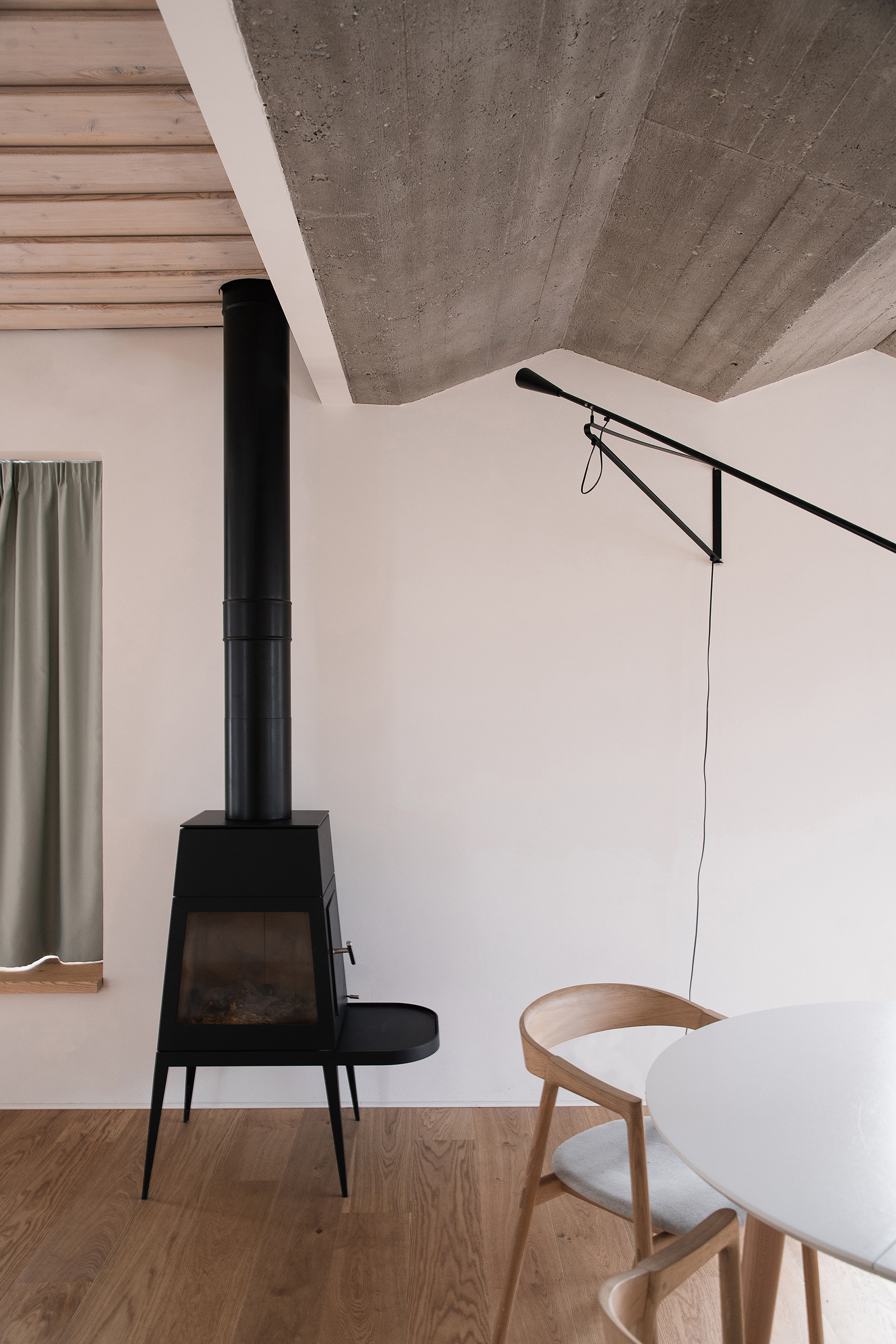 Black freestanding wood stove beneath exposed concrete ceiling with timber slat panels and a wall-mounted lamp