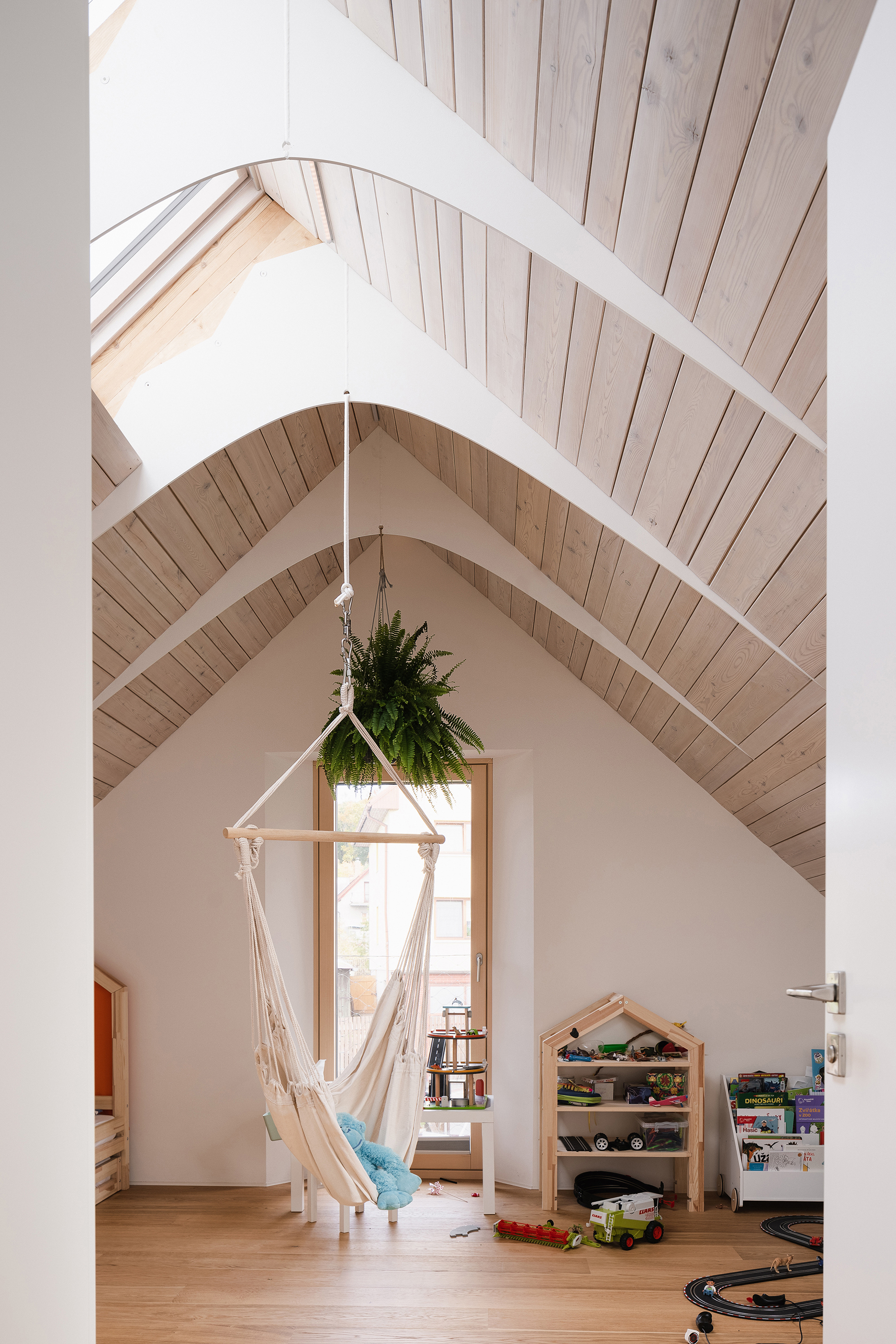 Gabled playroom with hanging macrame chair and timber ceiling framing a tall triangular window