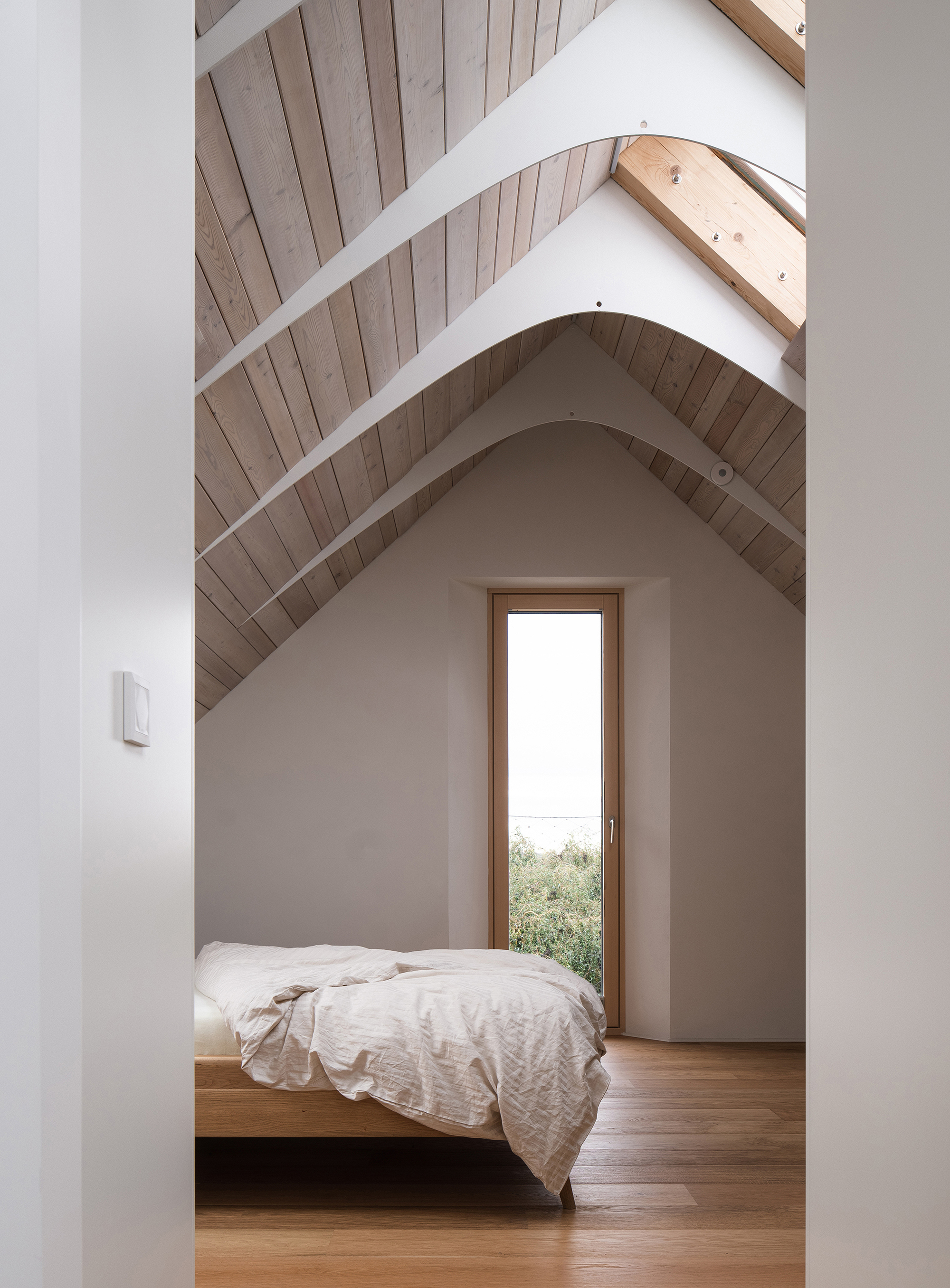 Bedroom with exposed timber rafters, tall narrow window and platform bed under vaulted ceiling