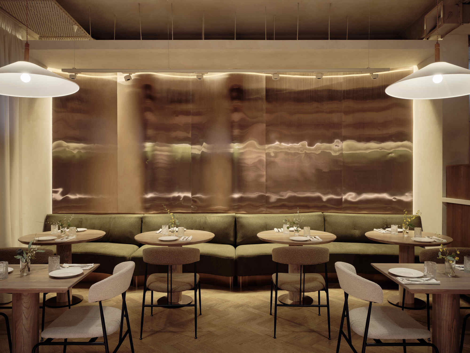 Banquette seating along translucent backlit wall panels with round tables and pendant lights overhead
