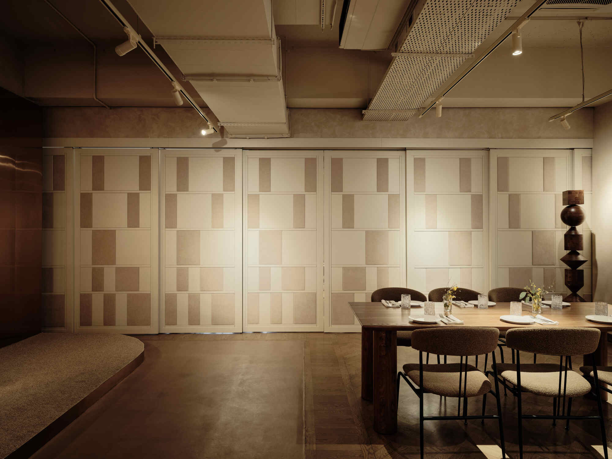 Folding panels with alternating wood tones beside a dining table and sculptural wooden floor lamp