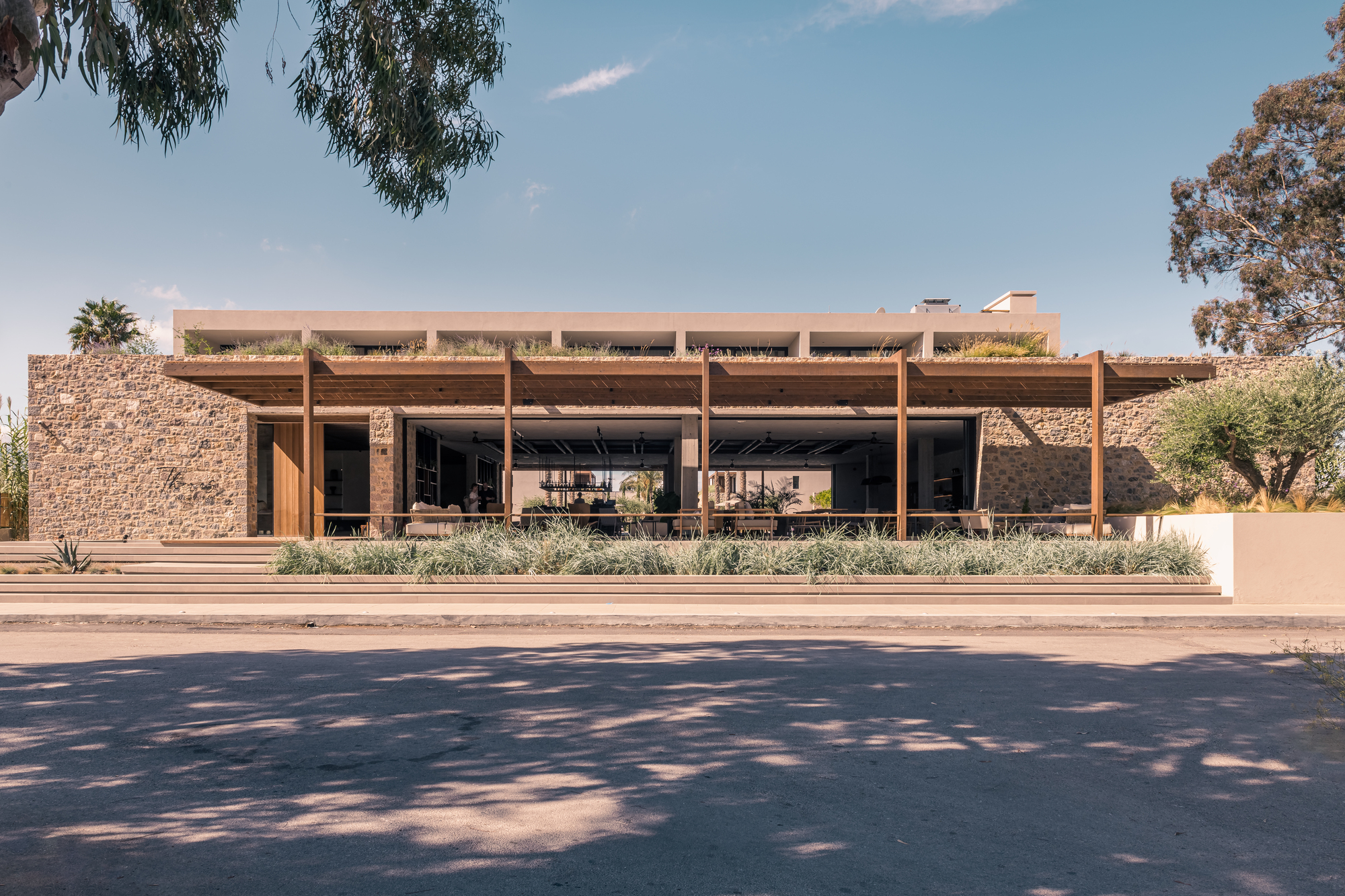 Street view of the timber pergola structure with planted beds framed by tree shadows on the pavement