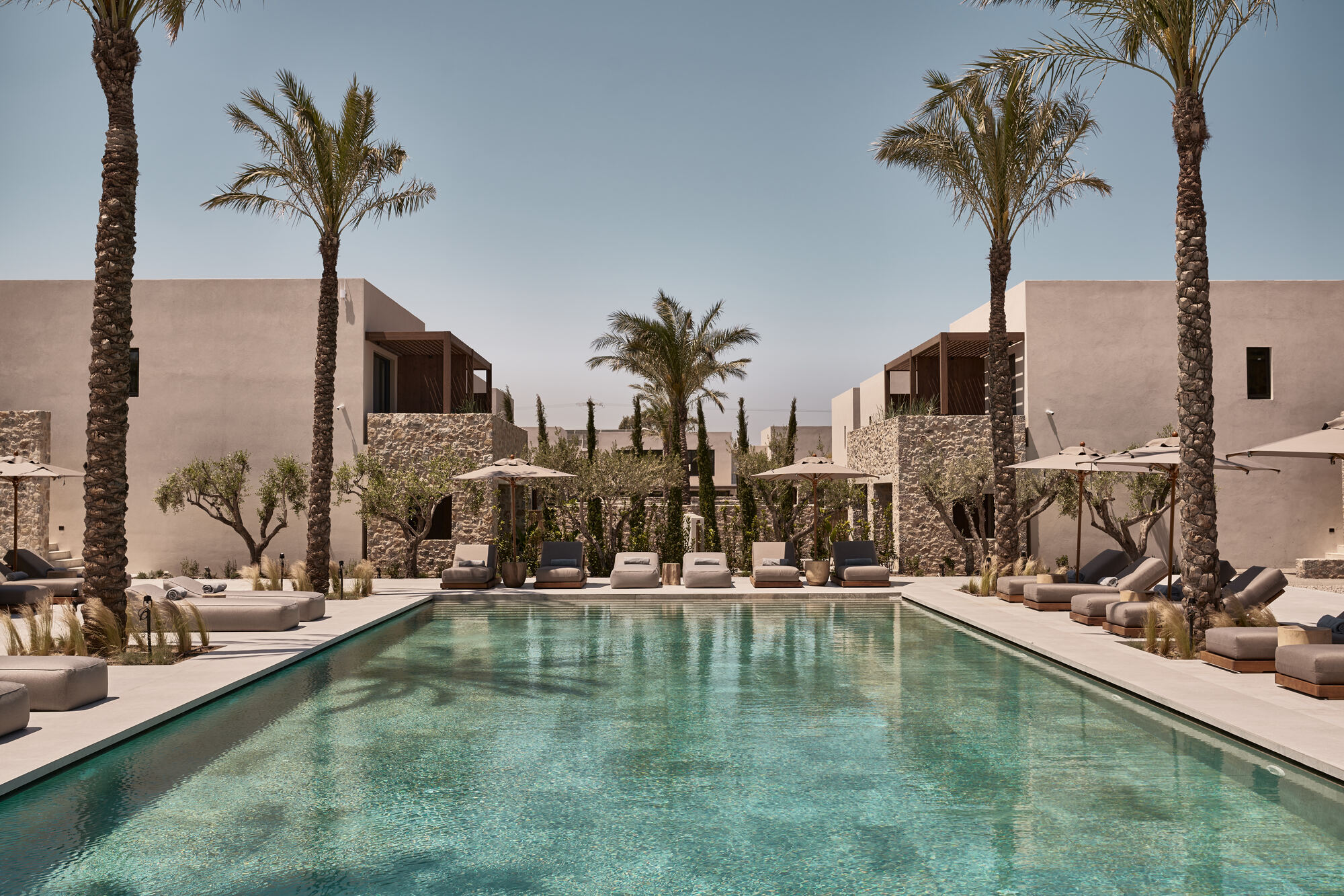 Central swimming pool flanked by symmetrical stone pergolas and lounge seating under palm trees