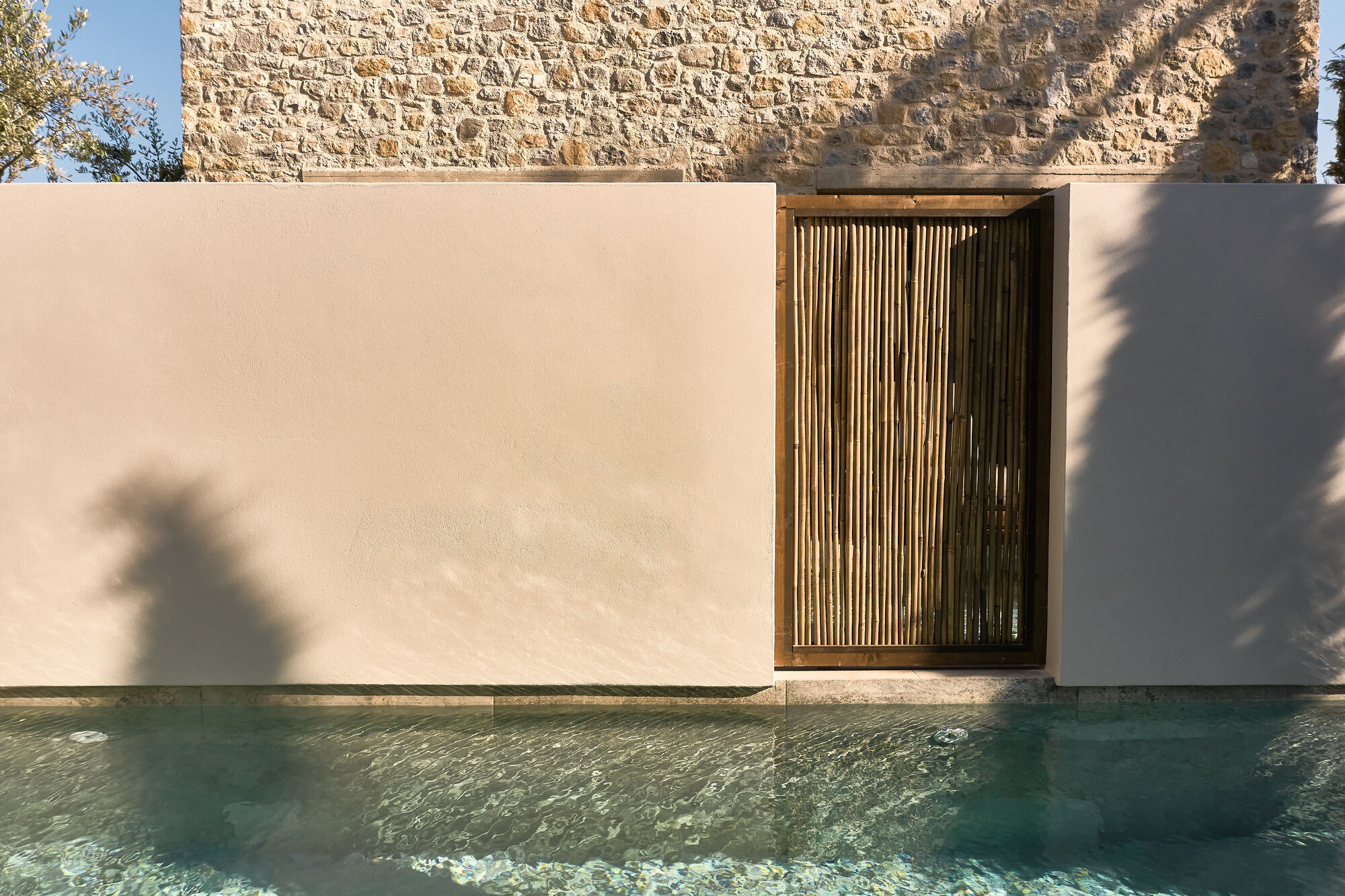 Vertical timber screen set in a rendered wall beside the pool edge casting afternoon shadows