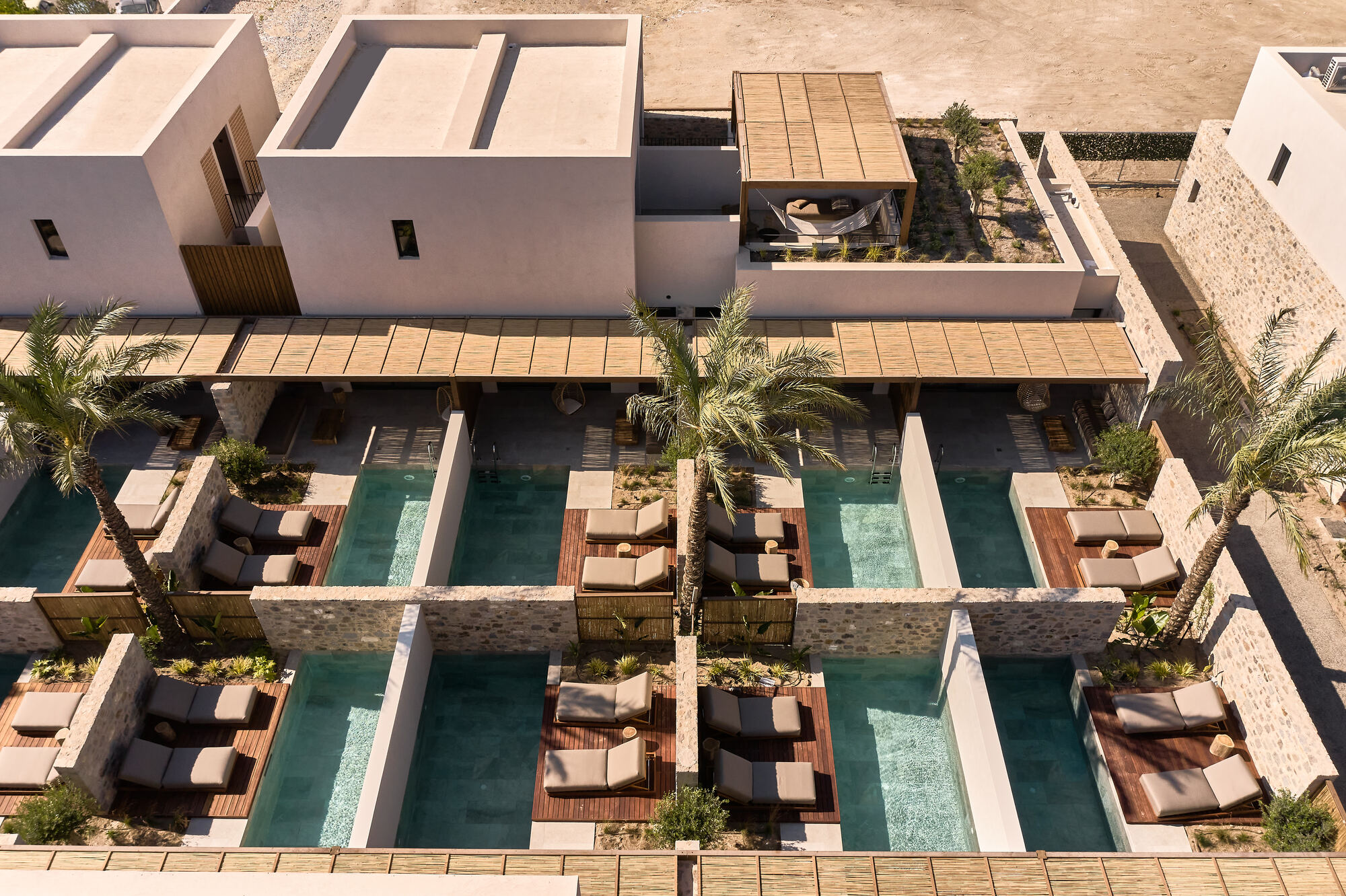 Aerial view of courtyard pools with timber decking and palm trees between white stucco volumes