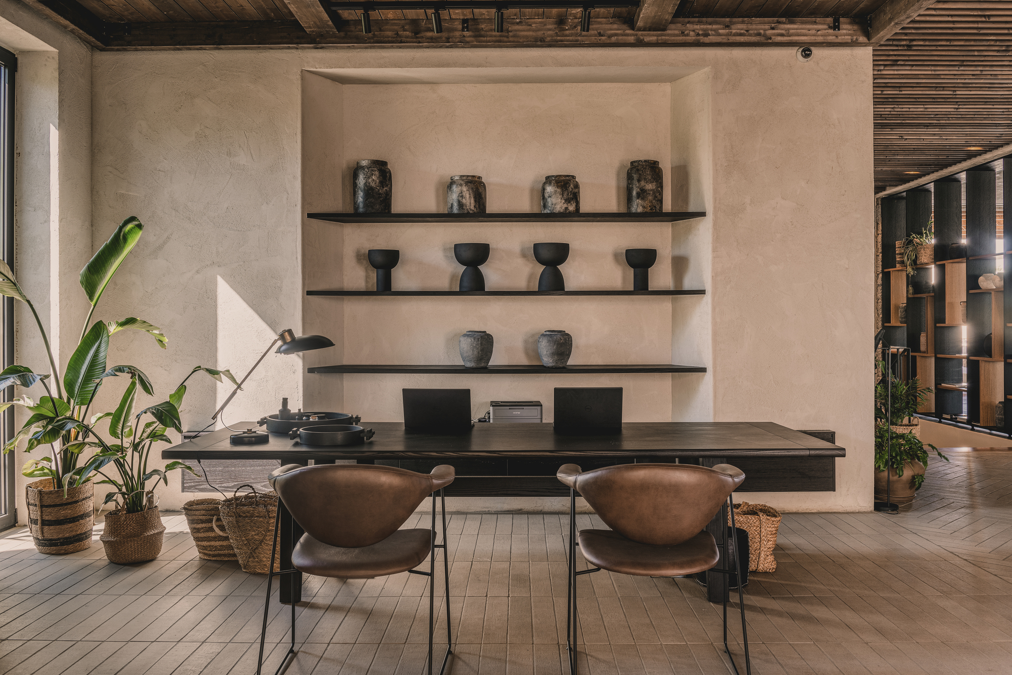 Dining area with black shelving displaying ceramics against a plastered wall beneath an exposed timber beam ceiling
