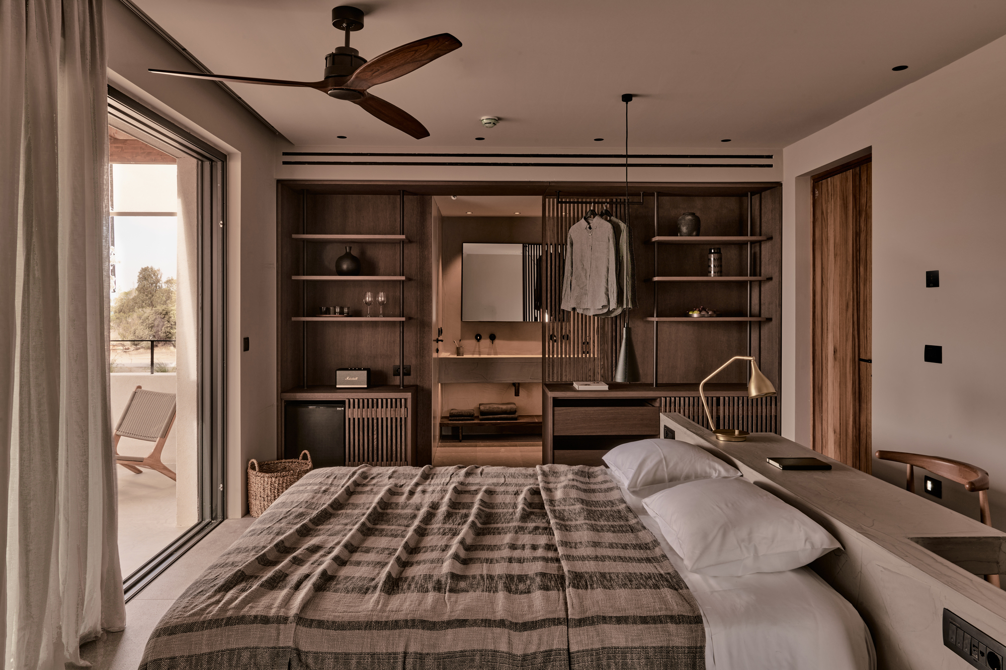 Bedroom with dark timber shelving unit and sliding glass doors opening to terrace with lone tree