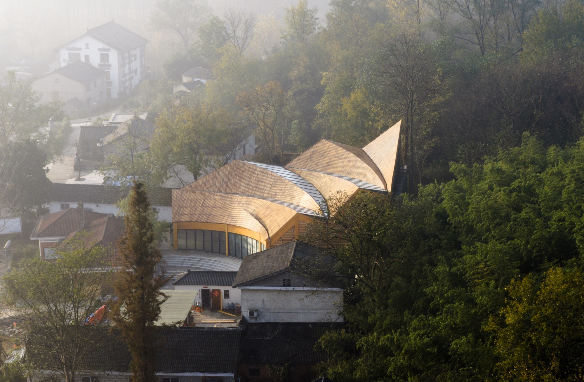 Elevated view of the three-lobed timber roof emerging from the hillside village in morning fog