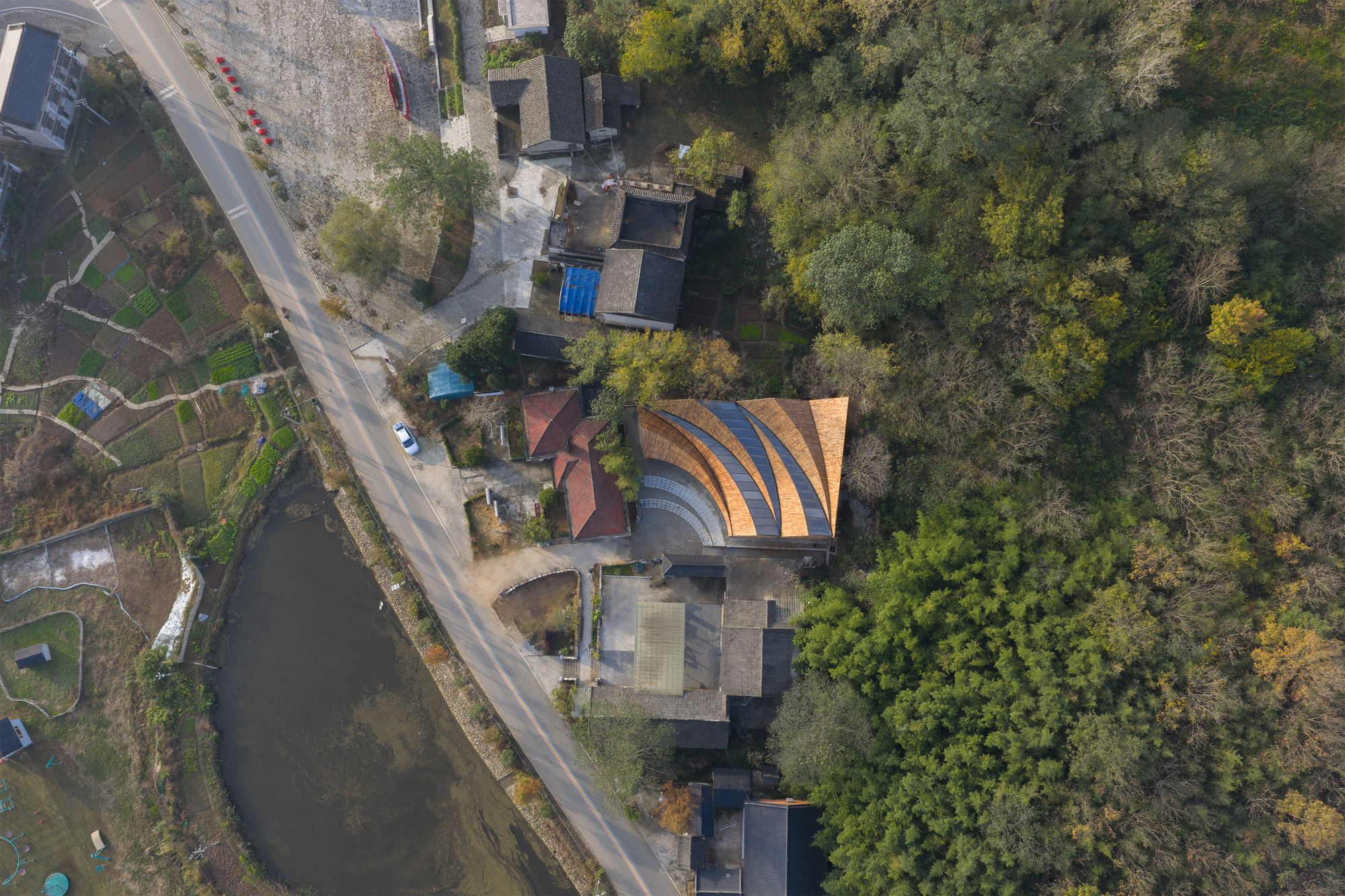 Overhead view showing the three-lobed timber roof beside a pond and residential buildings