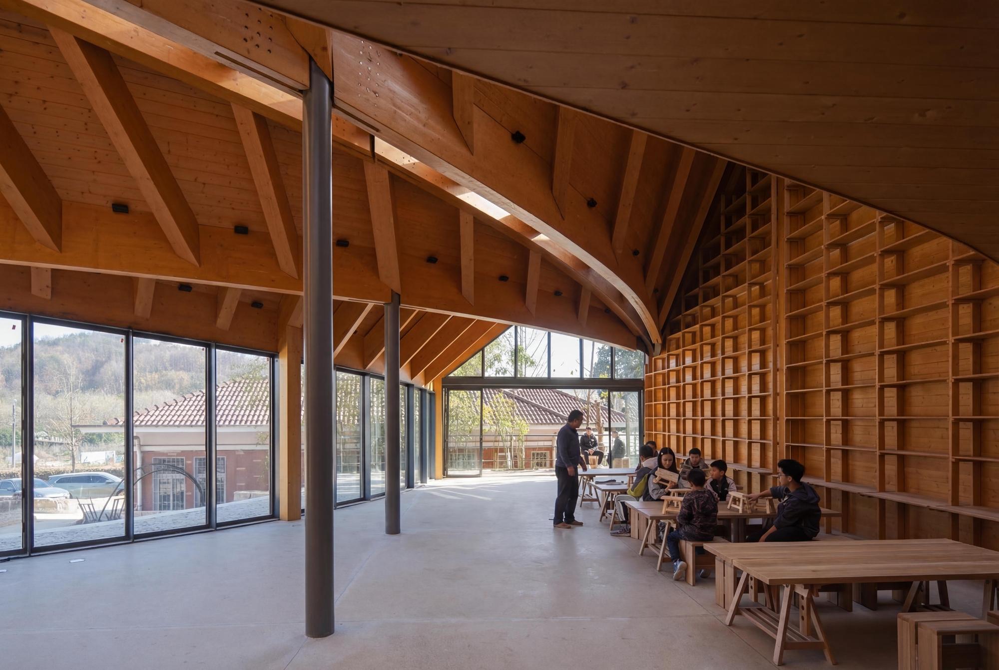 Open reading room with curved timber-grid wall, steel columns, and groups gathered at low tables