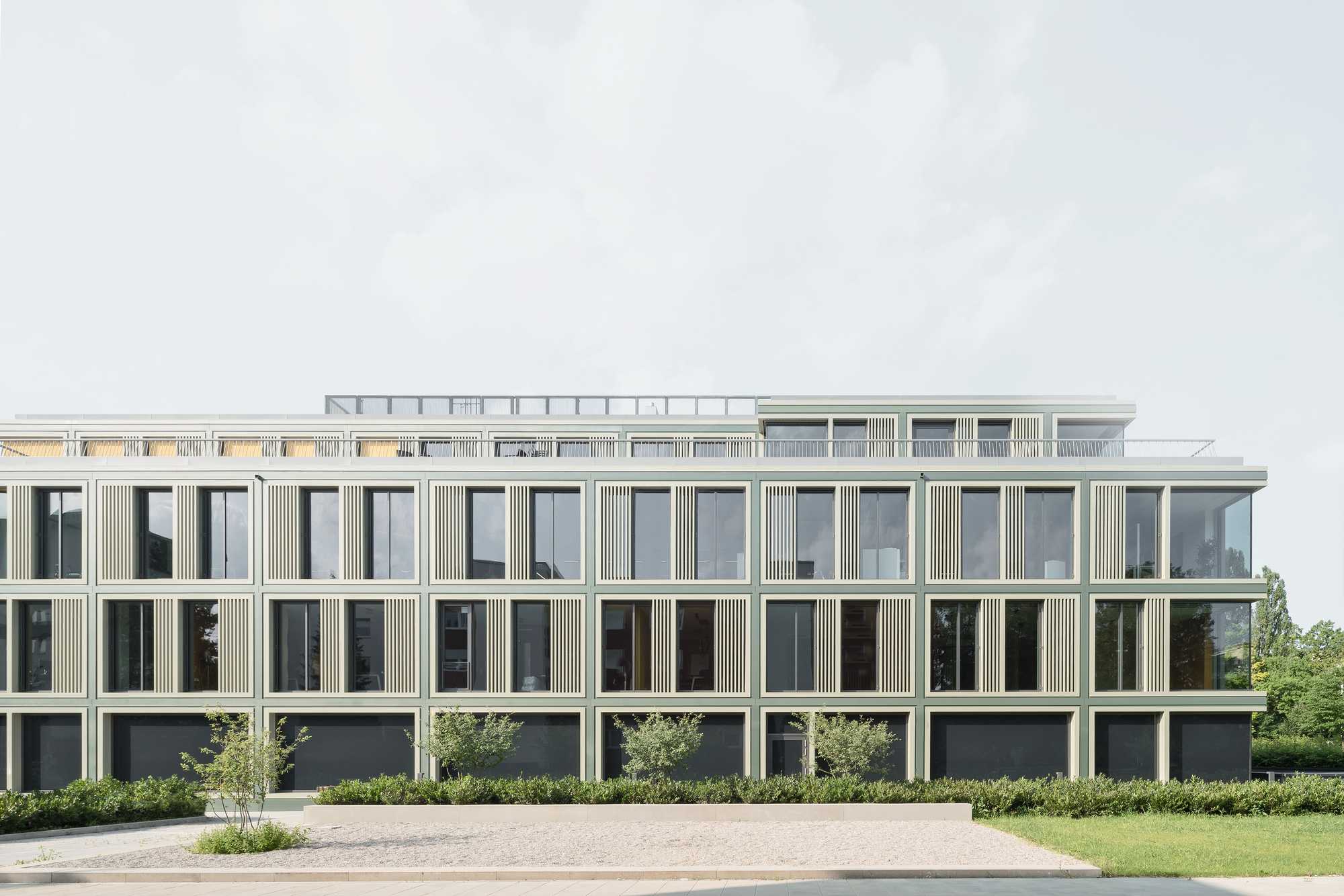 Long elevation showing repetitive grid of windows with vertical fin detailing and planted landscape below