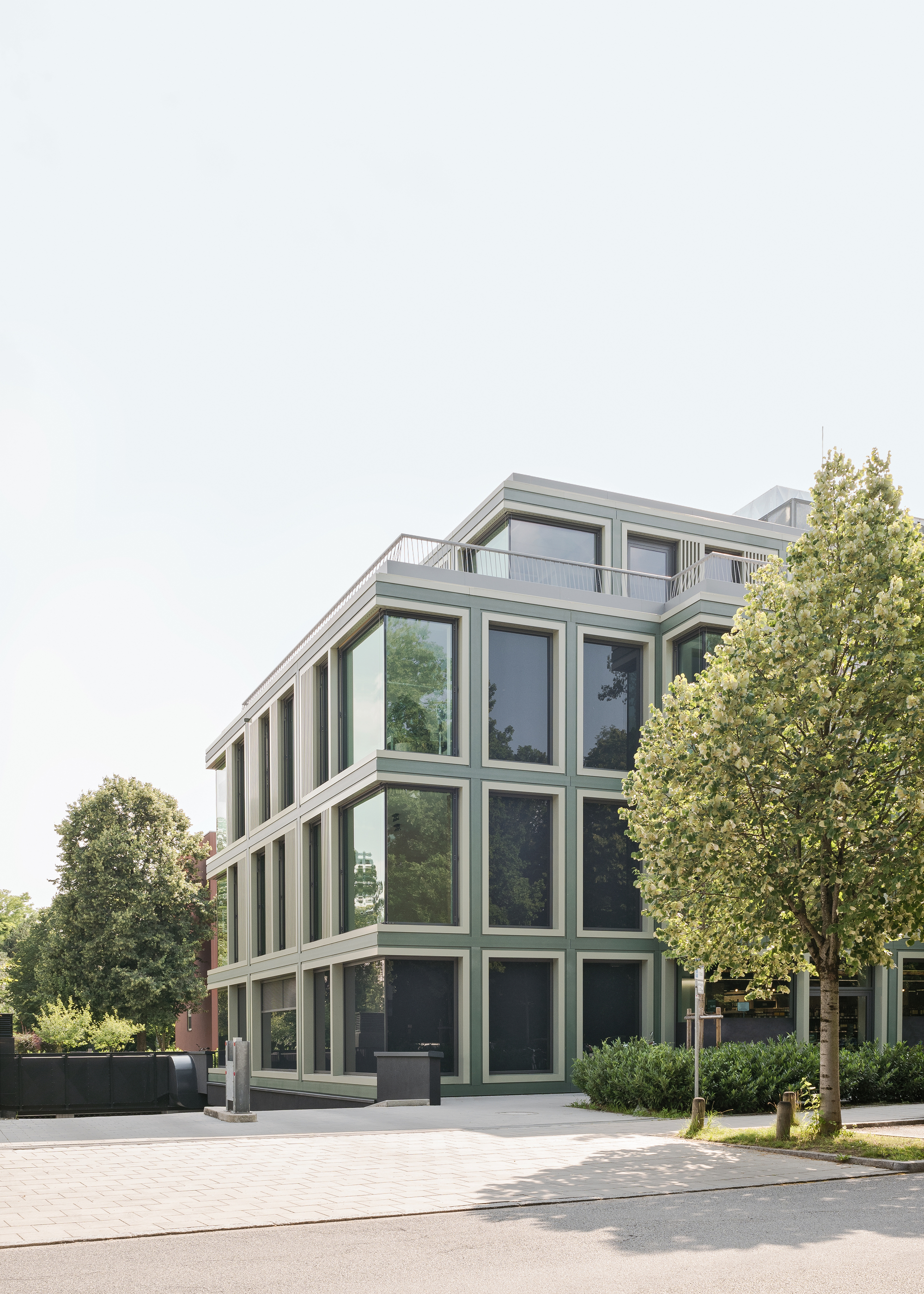 Street view of the glazed facade with vertical mullions framed by mature trees on a clear day