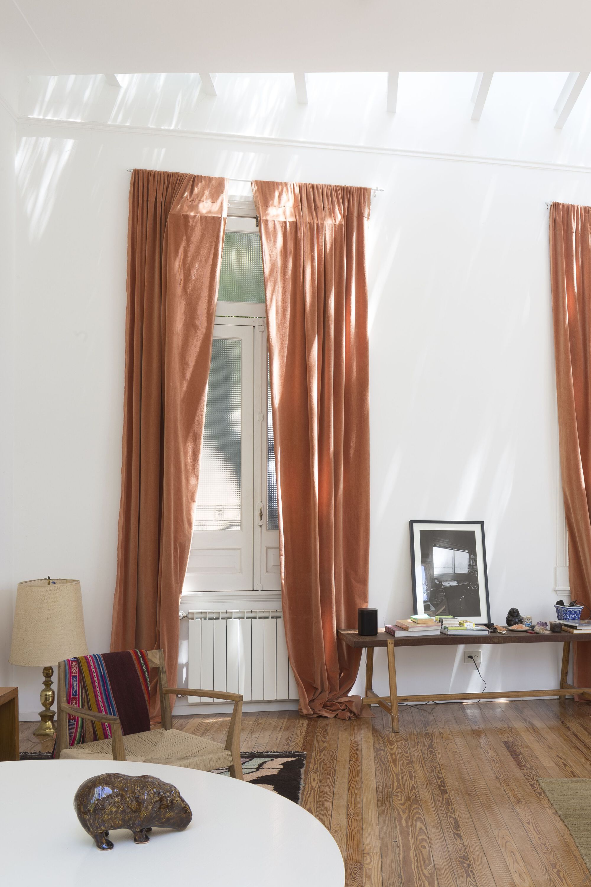 Interior room with terracotta curtains and sloped skylight ceiling casting sharp shadows across the floor