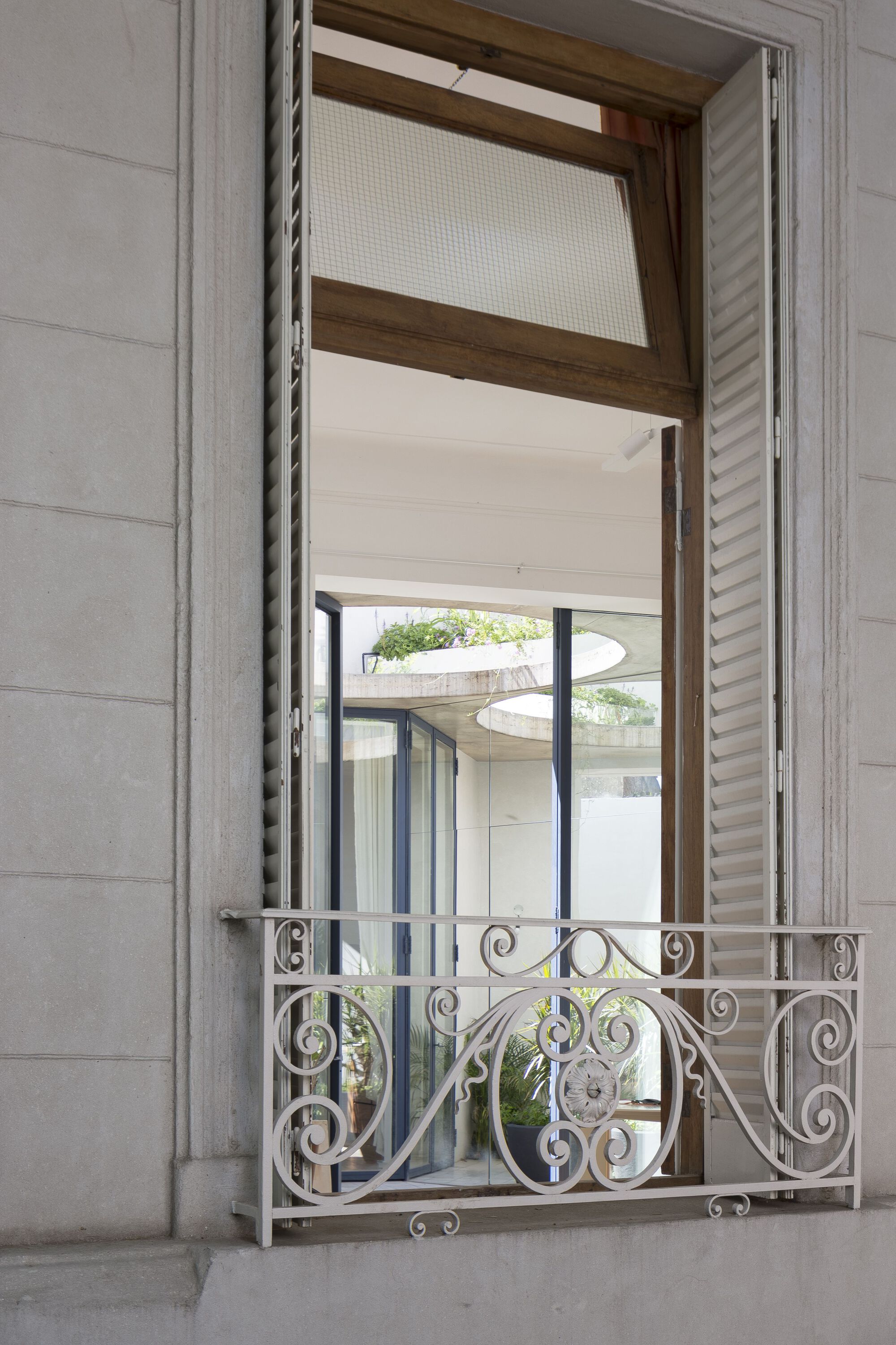 Open window with ornamental wrought iron balcony railing and timber frame looking into a planted courtyard