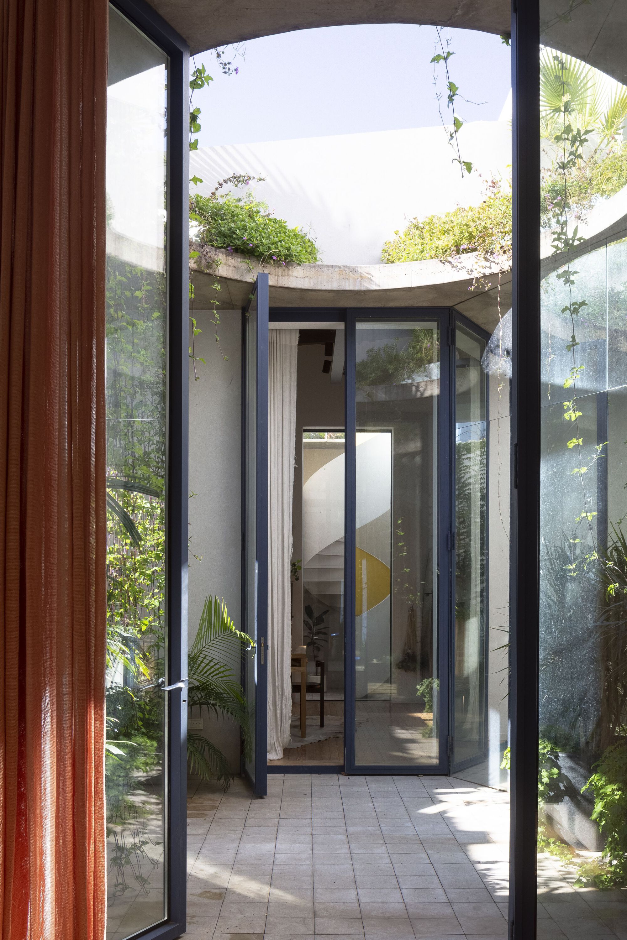 Glass doors opening from interior to a narrow courtyard with curved concrete planters overhead and tropical plants