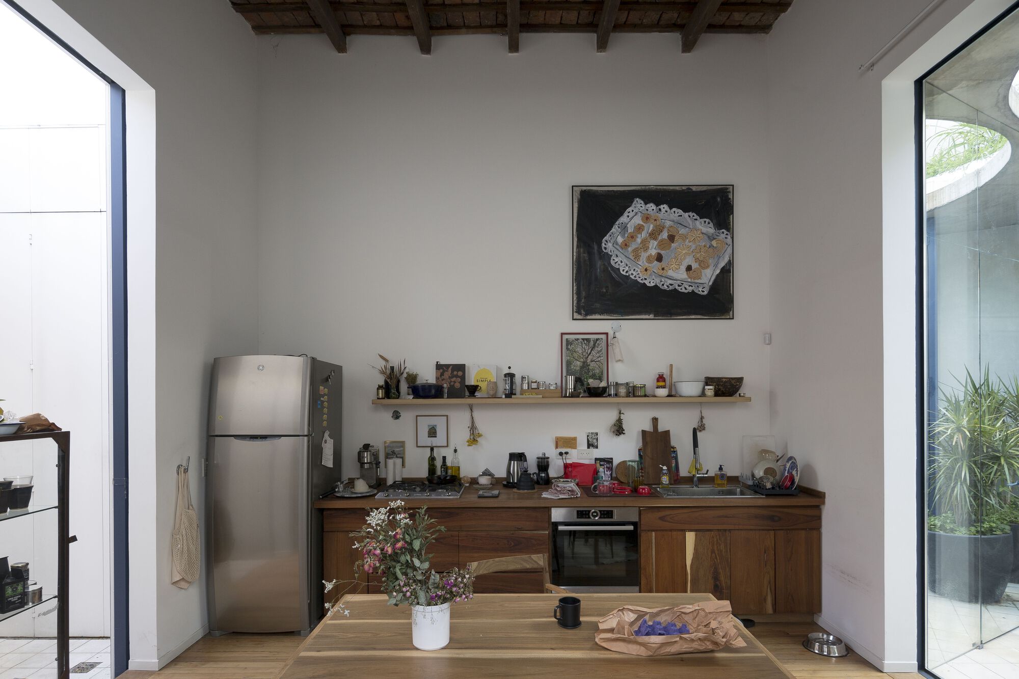 Kitchen with exposed timber beam ceiling, walnut cabinetry, and openings to planted courtyards on both sides