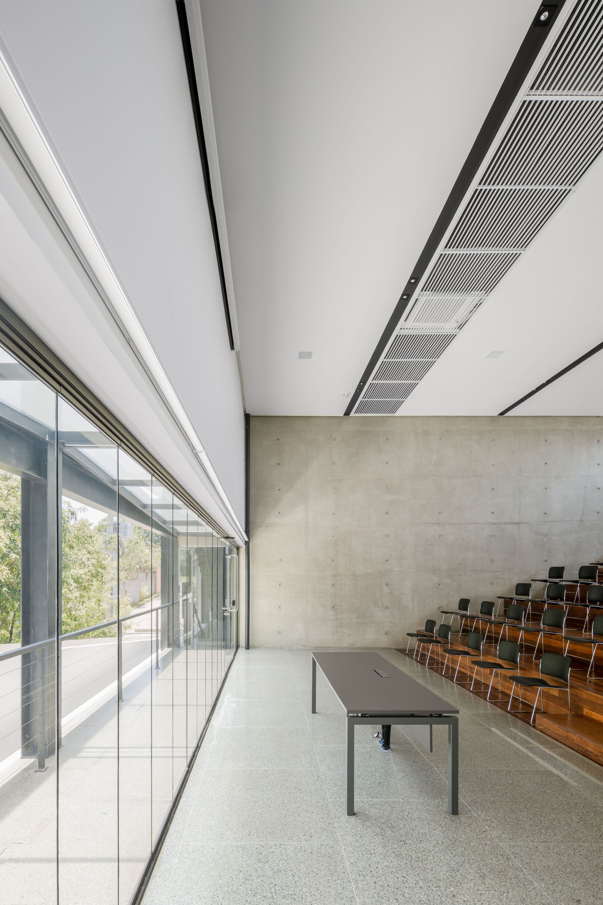 Interior assembly space with floor-to-ceiling glass wall, concrete backdrop and tiered wooden seating