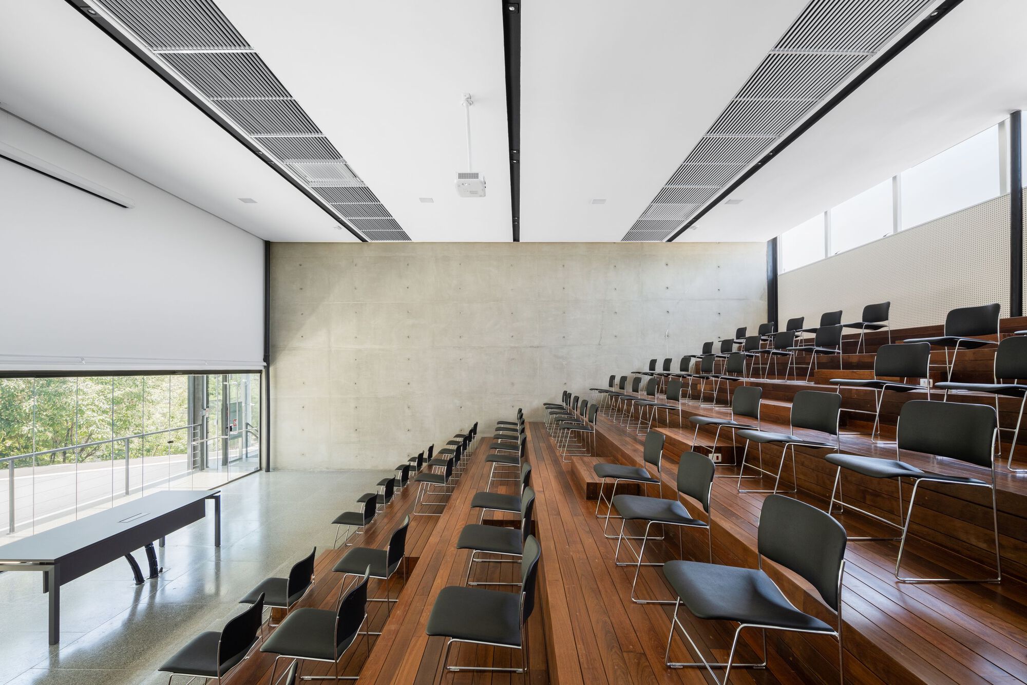 Tiered timber auditorium seating facing a board-formed concrete wall with clerestory windows above