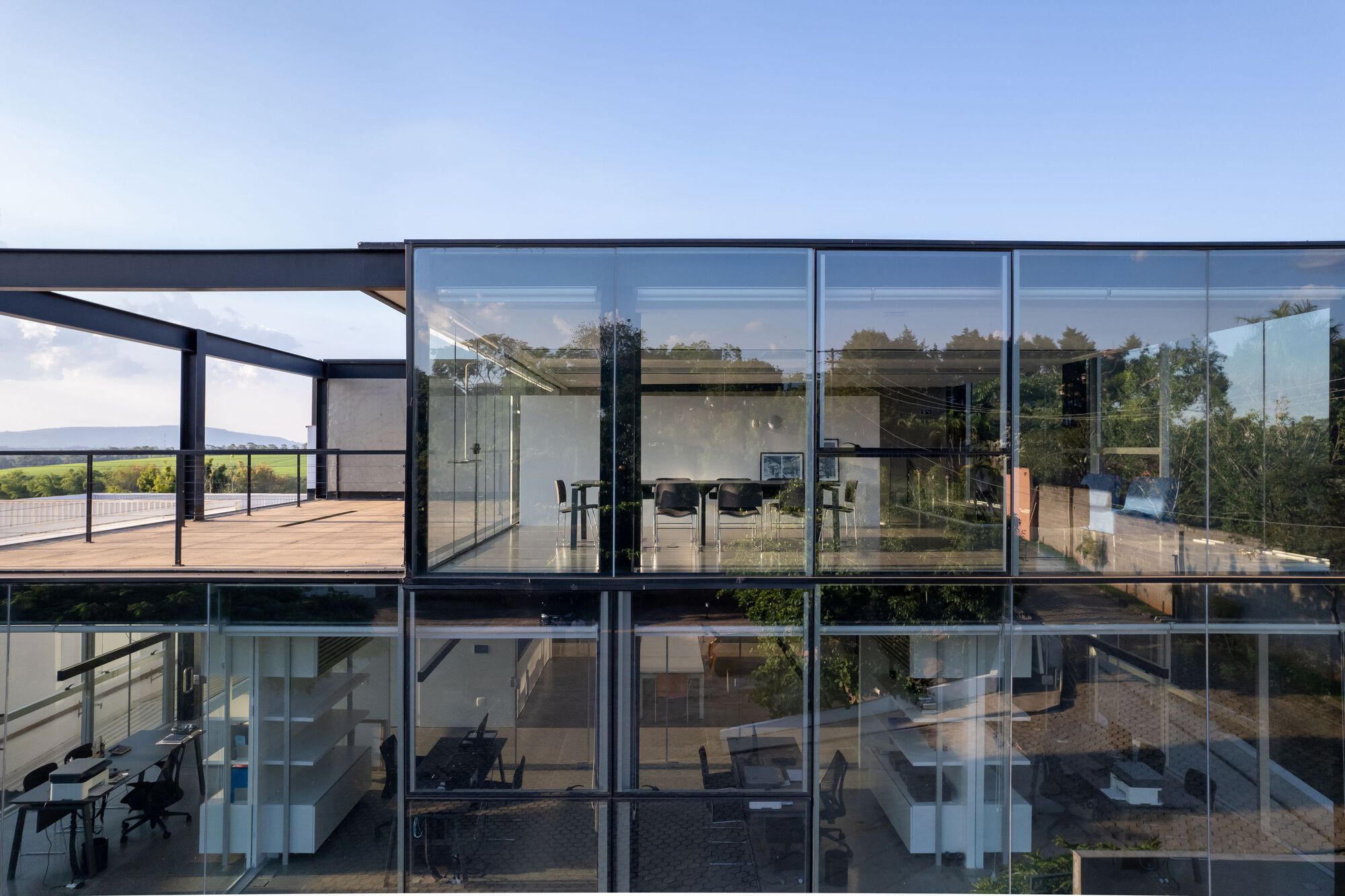 Two-storey glazed facade reflecting trees and sky with timber deck at upper level