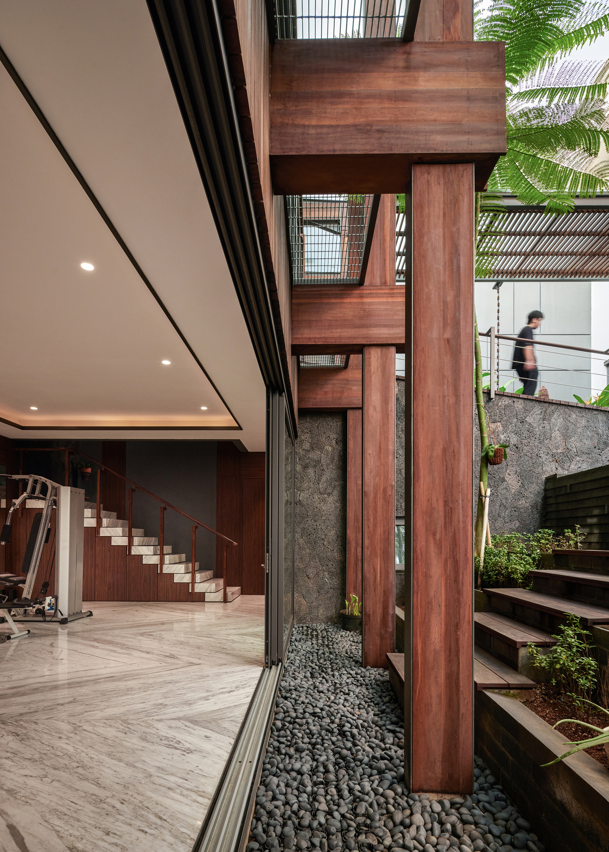 Vertical timber slat screen beside an interior courtyard with black river stones and a figure on the upper level