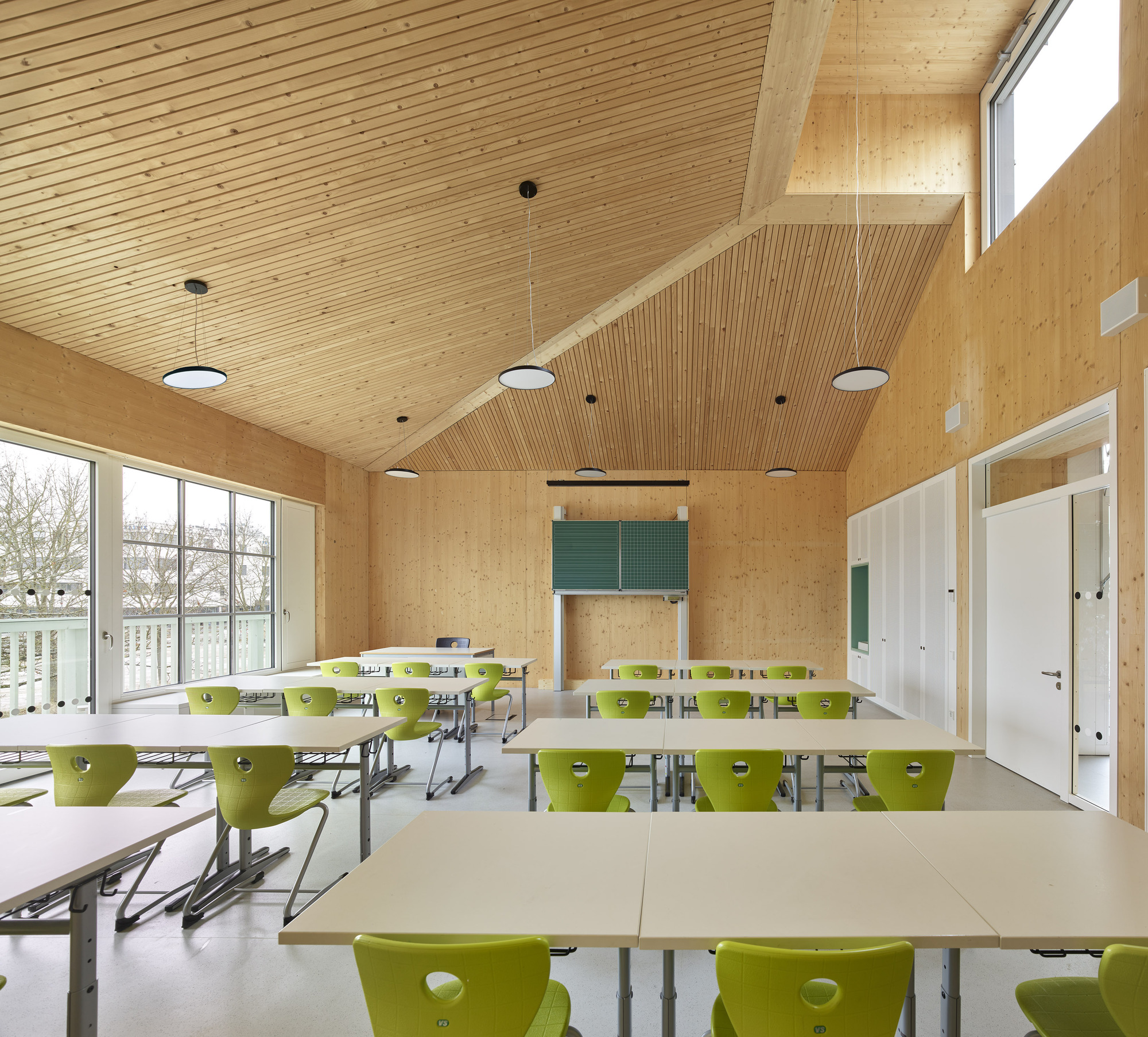 Classroom with lime green chairs at white tables under a slatted timber ceiling