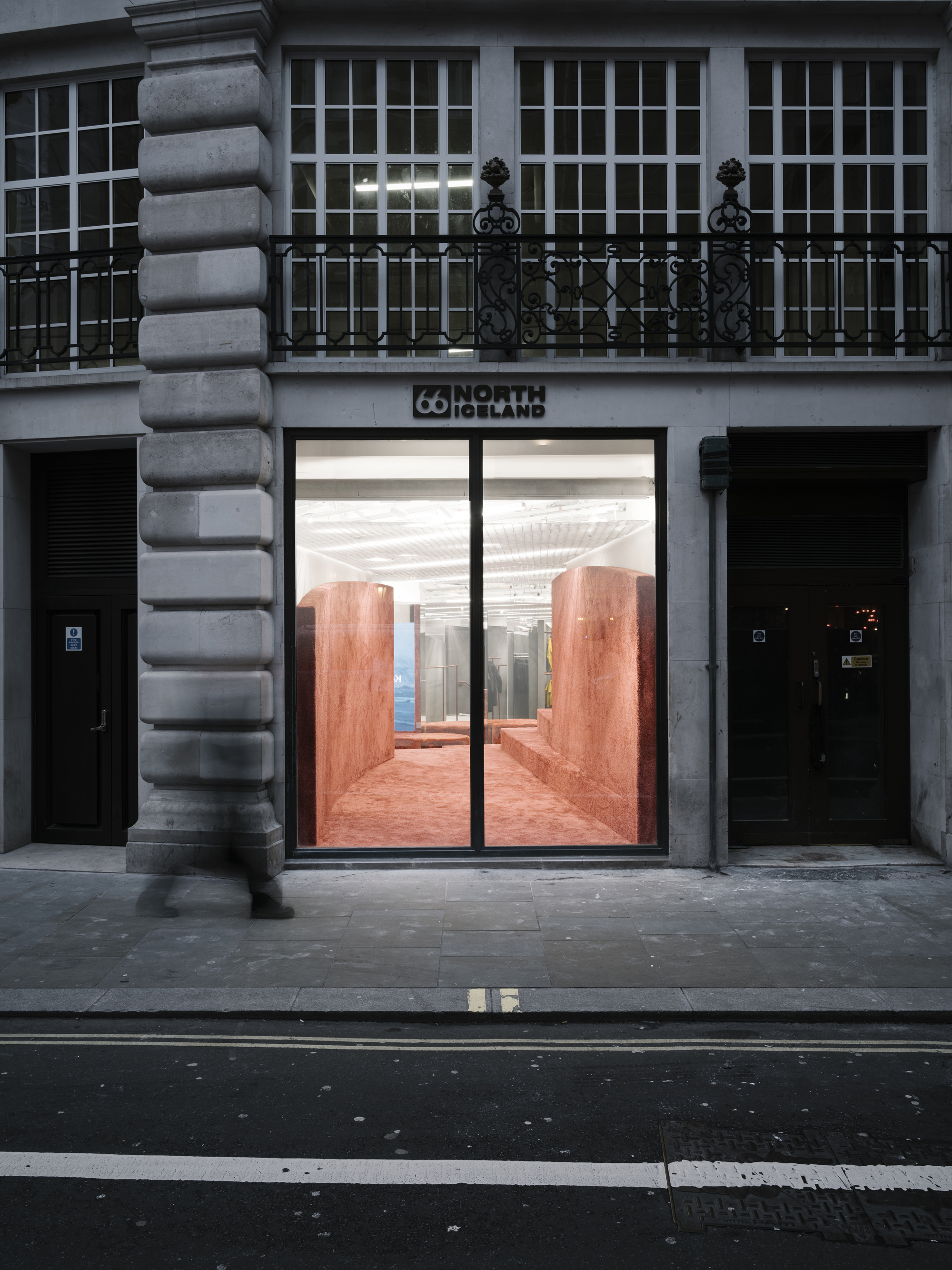 Street-level storefront with glass doors framing red textured walls visible from a rusticated stone facade