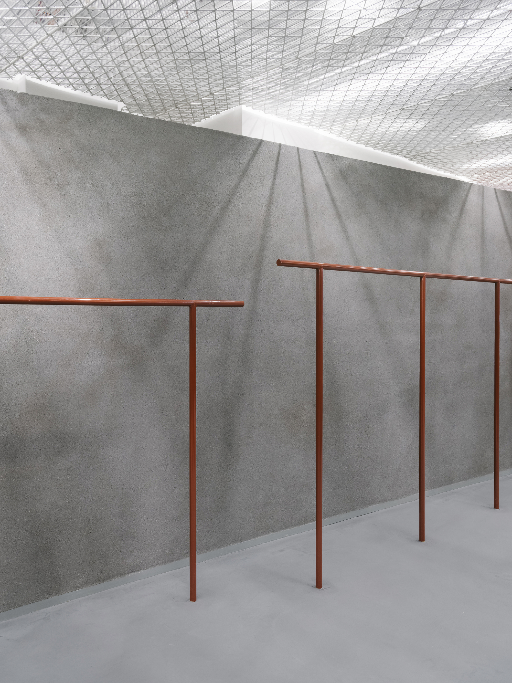 Close-up of copper-toned tubular railings against a folded grey concrete wall catching soft shadows