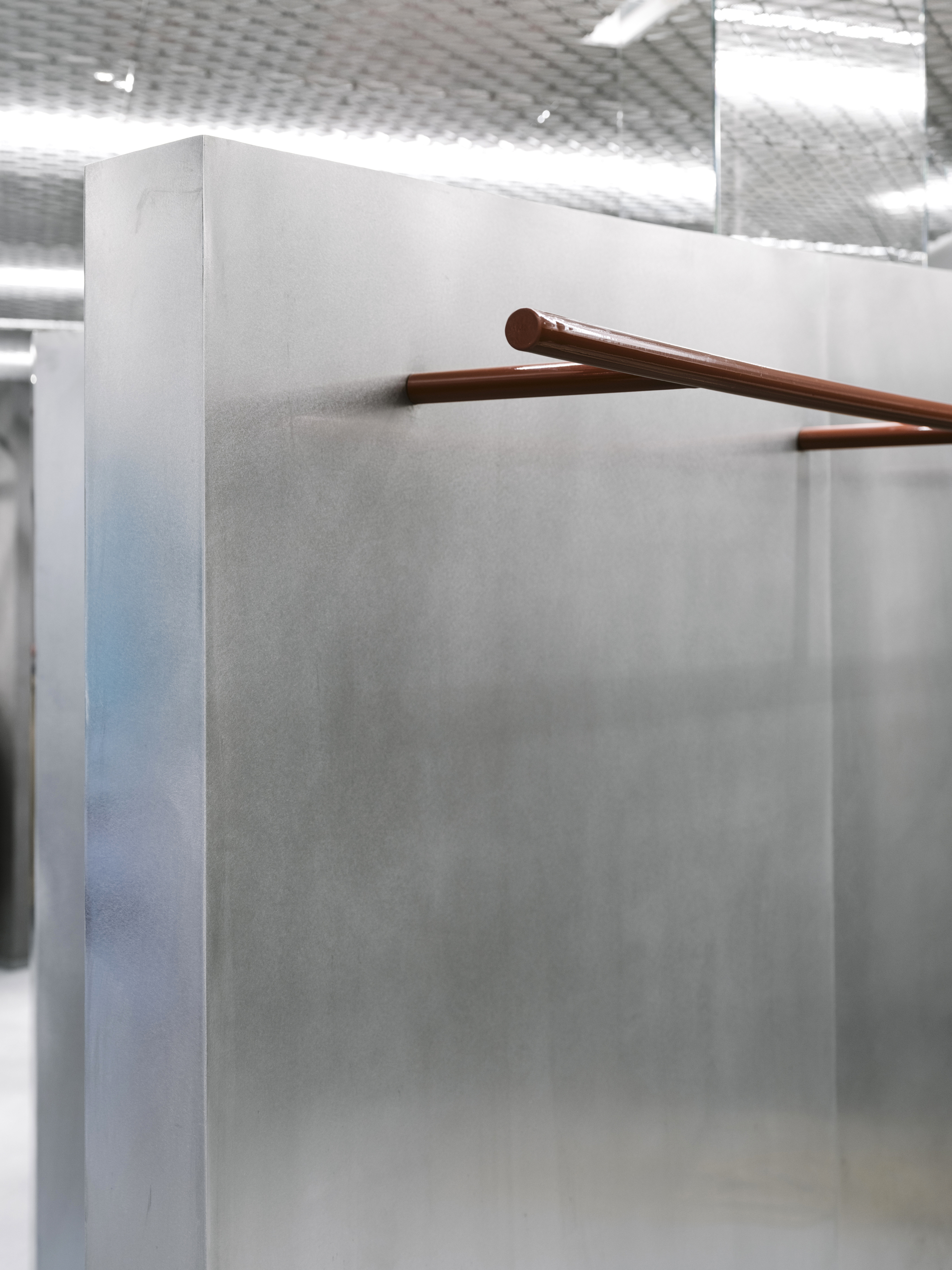 Close-up of a copper handrail extending from a grey concrete partition under diffused ceiling light