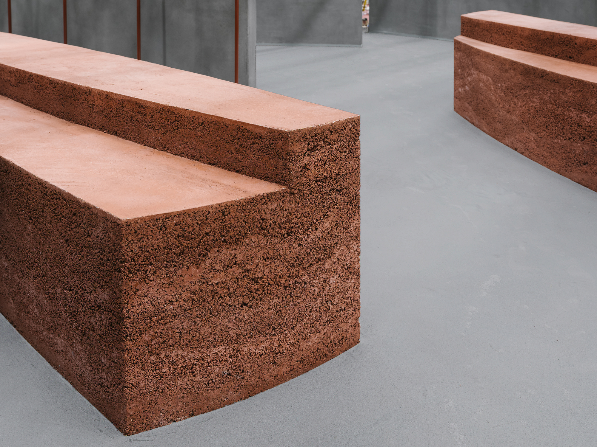 Red volcanic aggregate concrete bench with smooth top surface on a grey polished floor