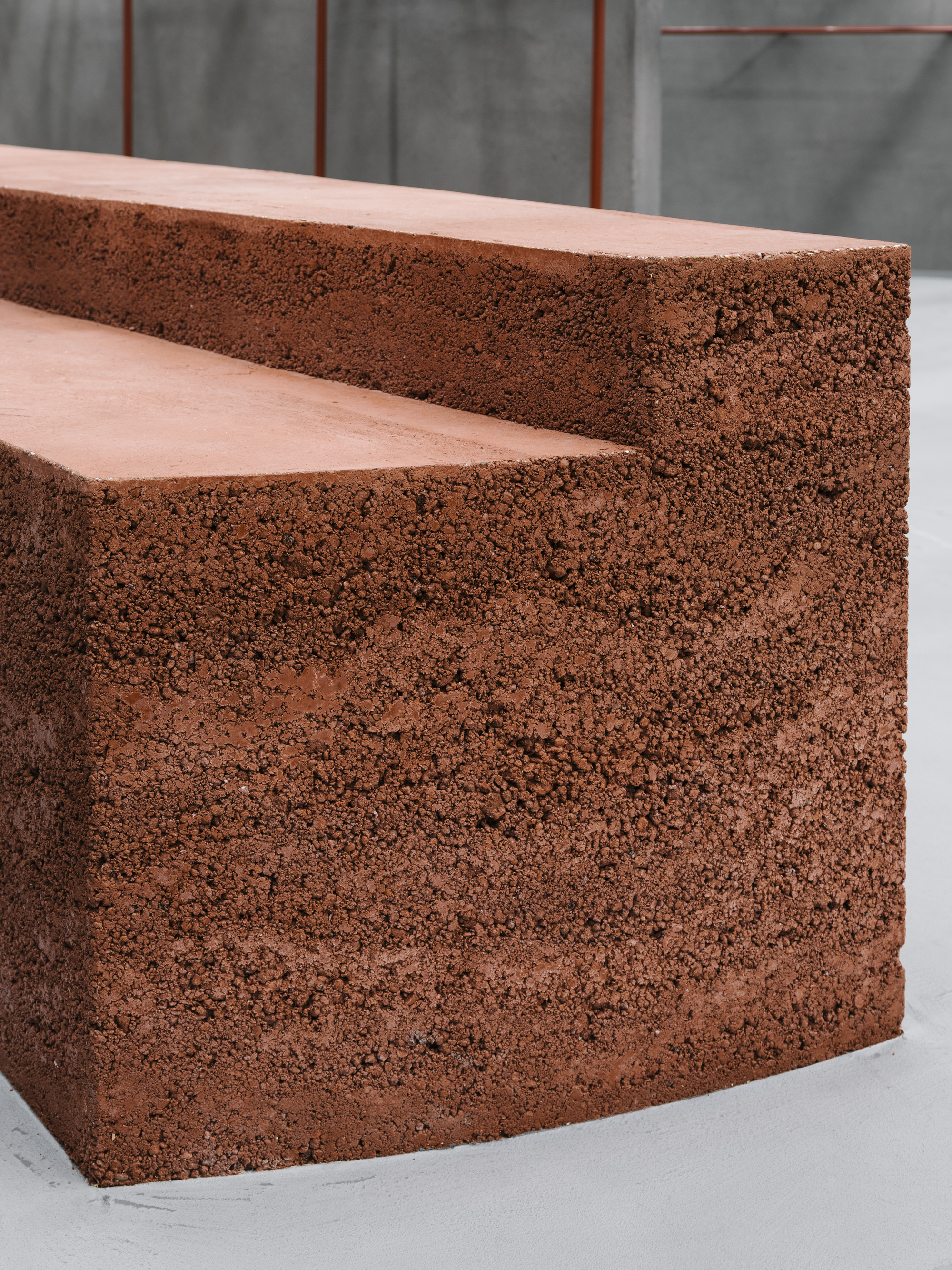 Close-up of reddish porous aggregate steps with smooth tread surfaces against a grey concrete backdrop