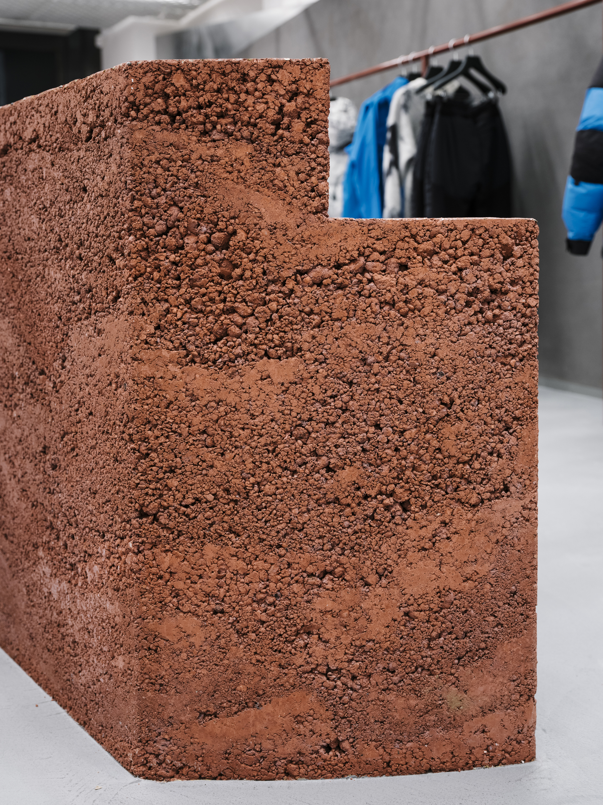 Curved reddish aggregate stair detail with clothing rack visible in the background space
