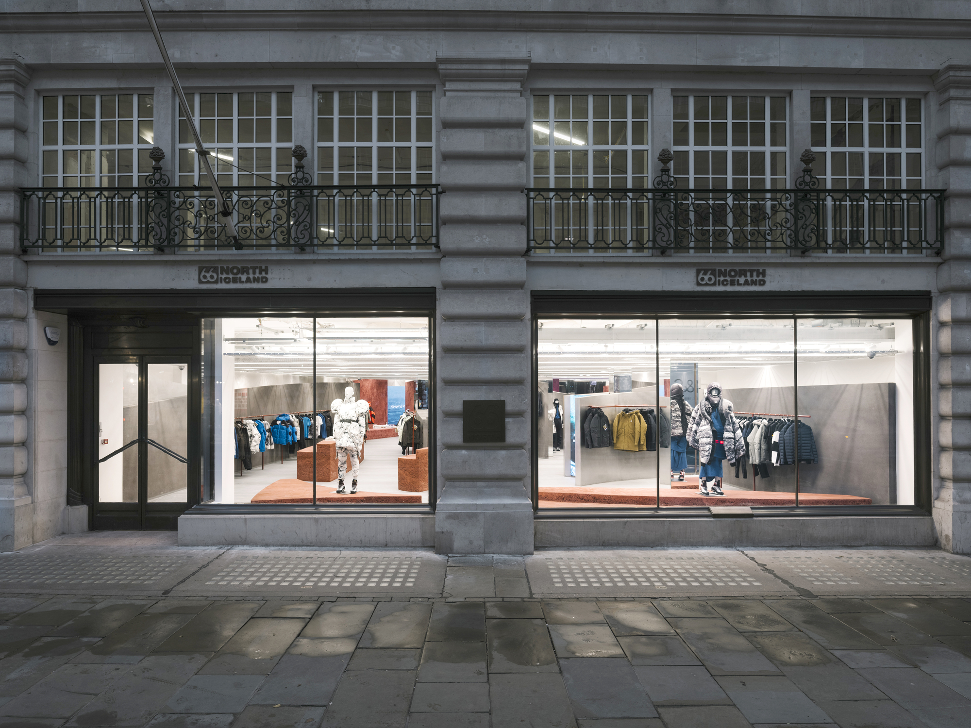 Street facade showing twin storefronts with large glazing below ornamental balconies on grey stone building