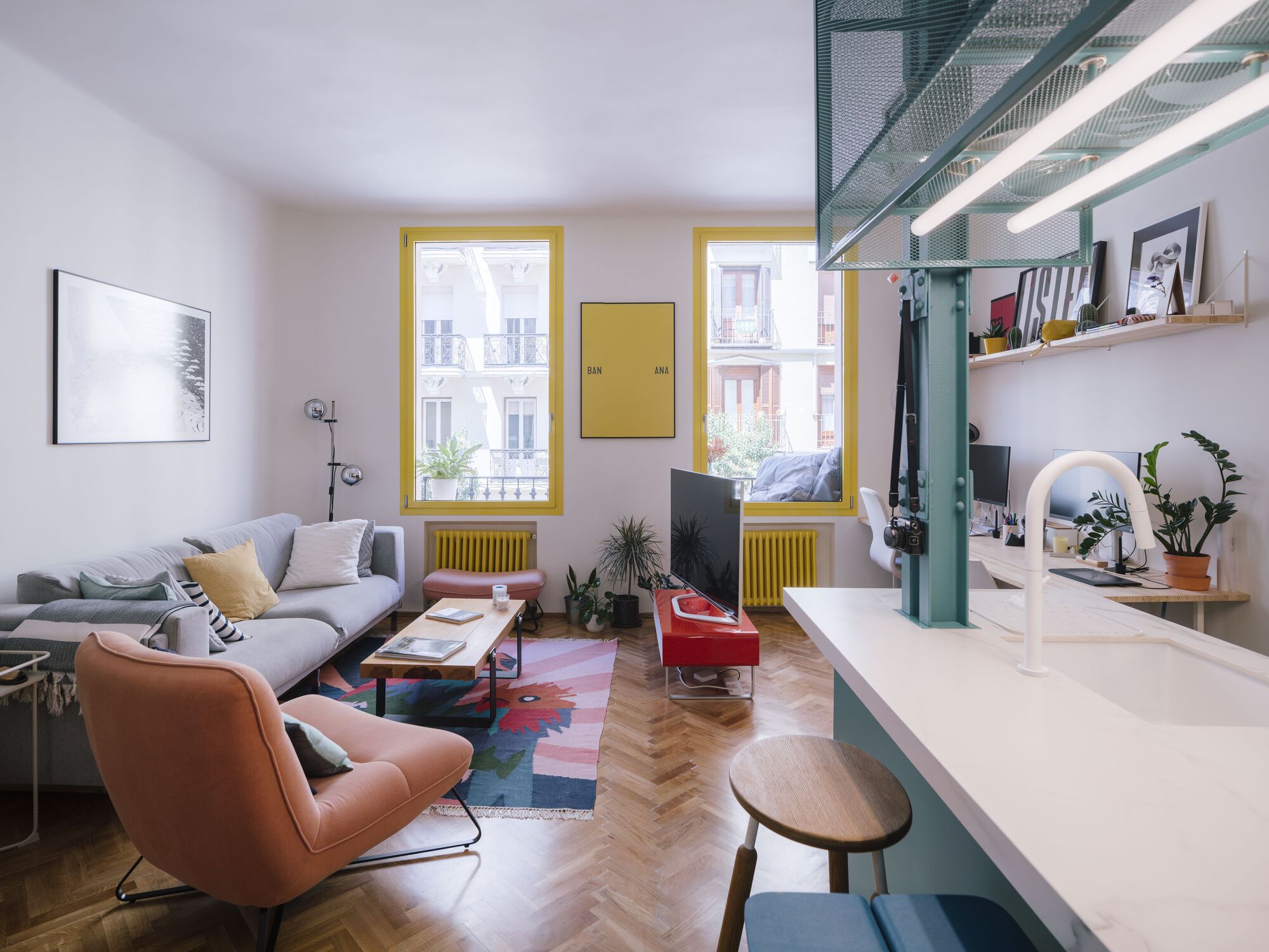Open living area with yellow-framed windows, teal kitchen island and herringbone wood flooring in daylight