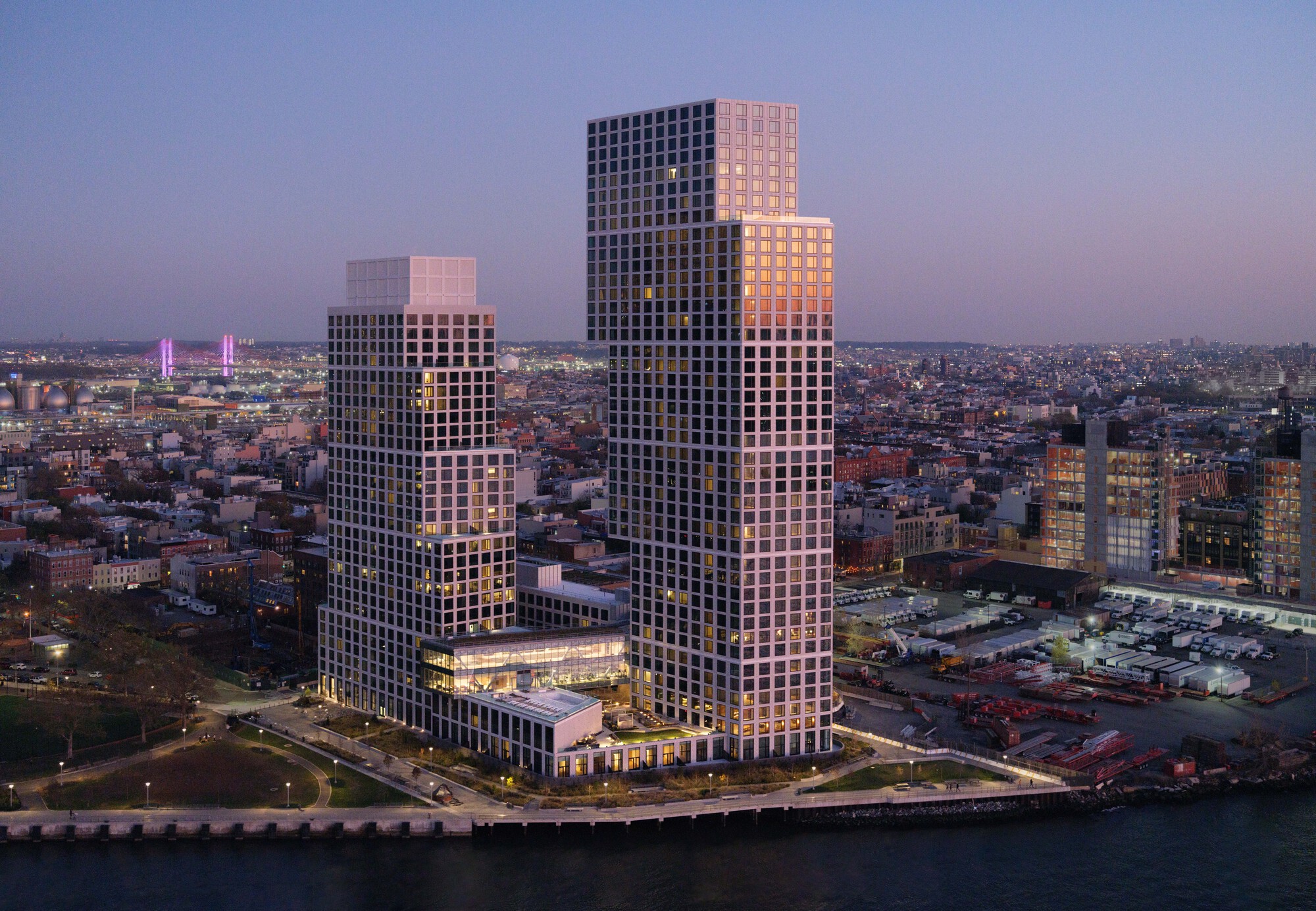 Aerial view of the stacked tower volumes at dusk with illuminated windows and distant skyline