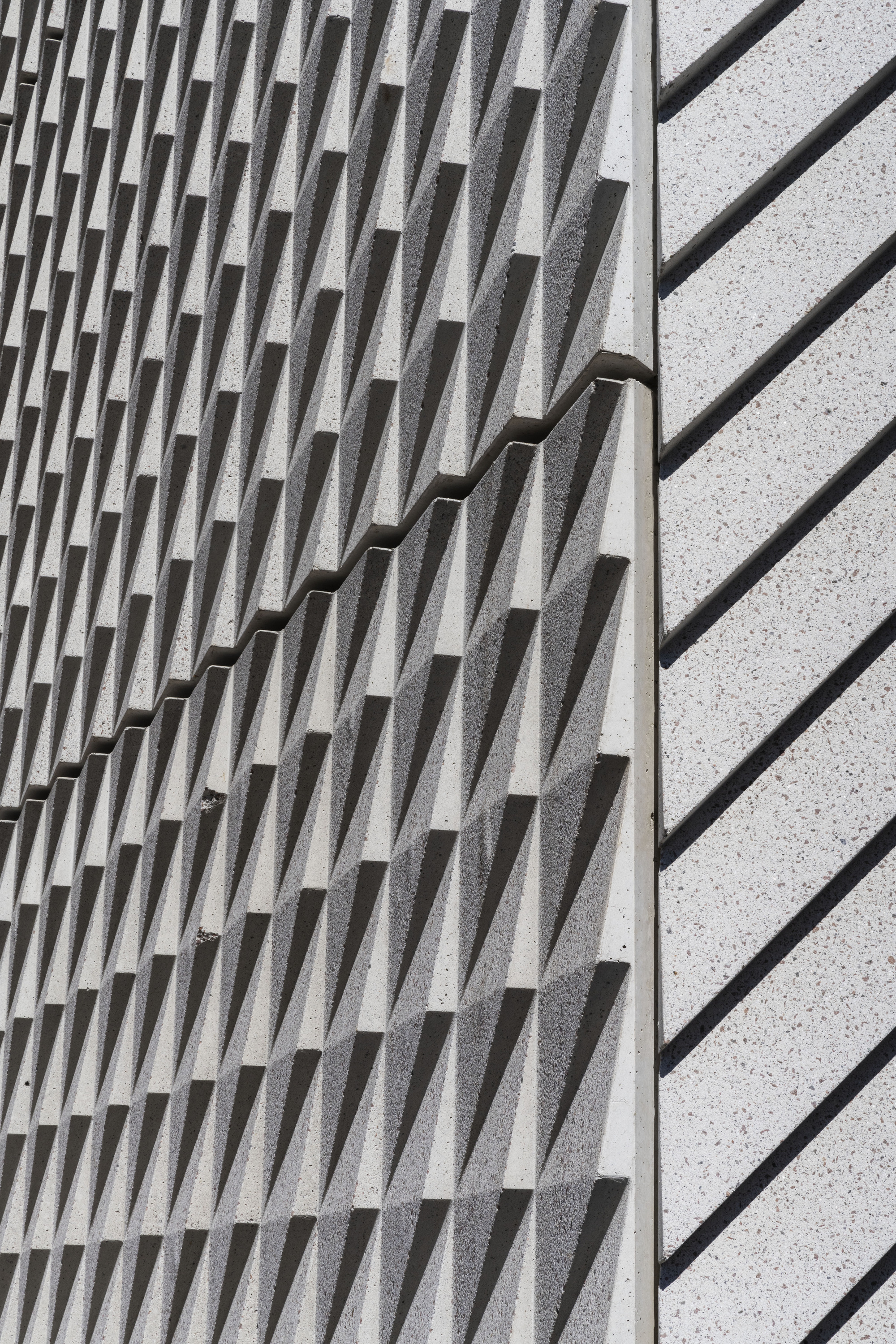 Close-up of textured concrete wall with protruding vertical fins meeting a smooth terrazzo surface