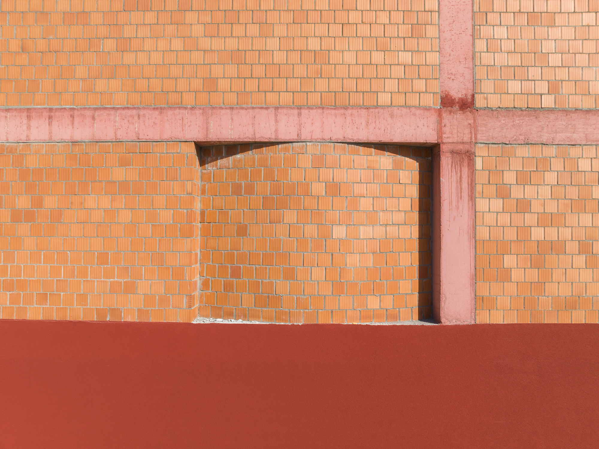 Detail of arched opening in terracotta brick wall with pink concrete structural frame