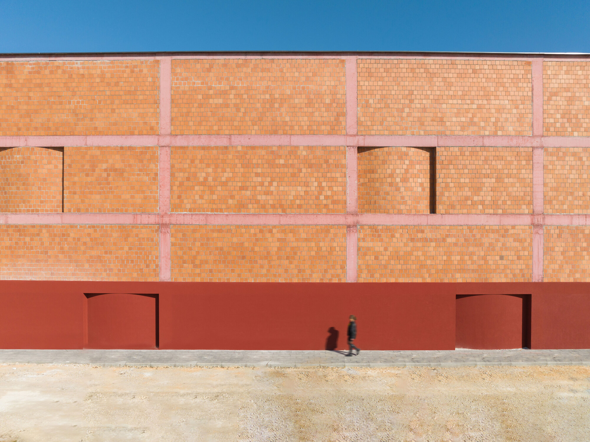 Facade with two doorways in red plaster base below upper terracotta brick wall as figure walks past