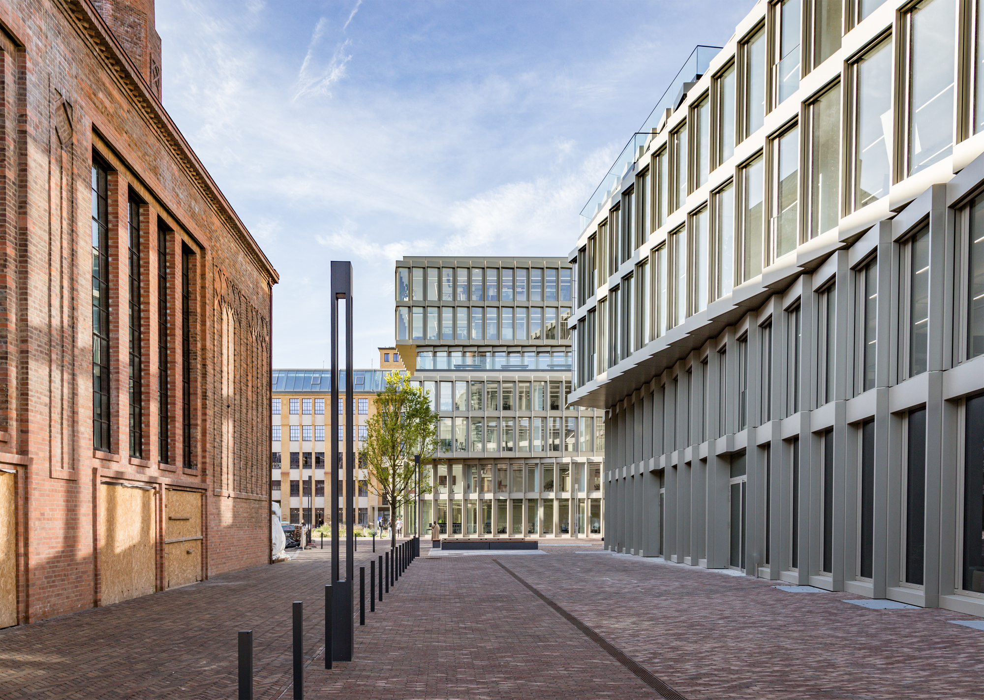 Pedestrian passage between red brick historic wall and new glass facade with vertical louvres
