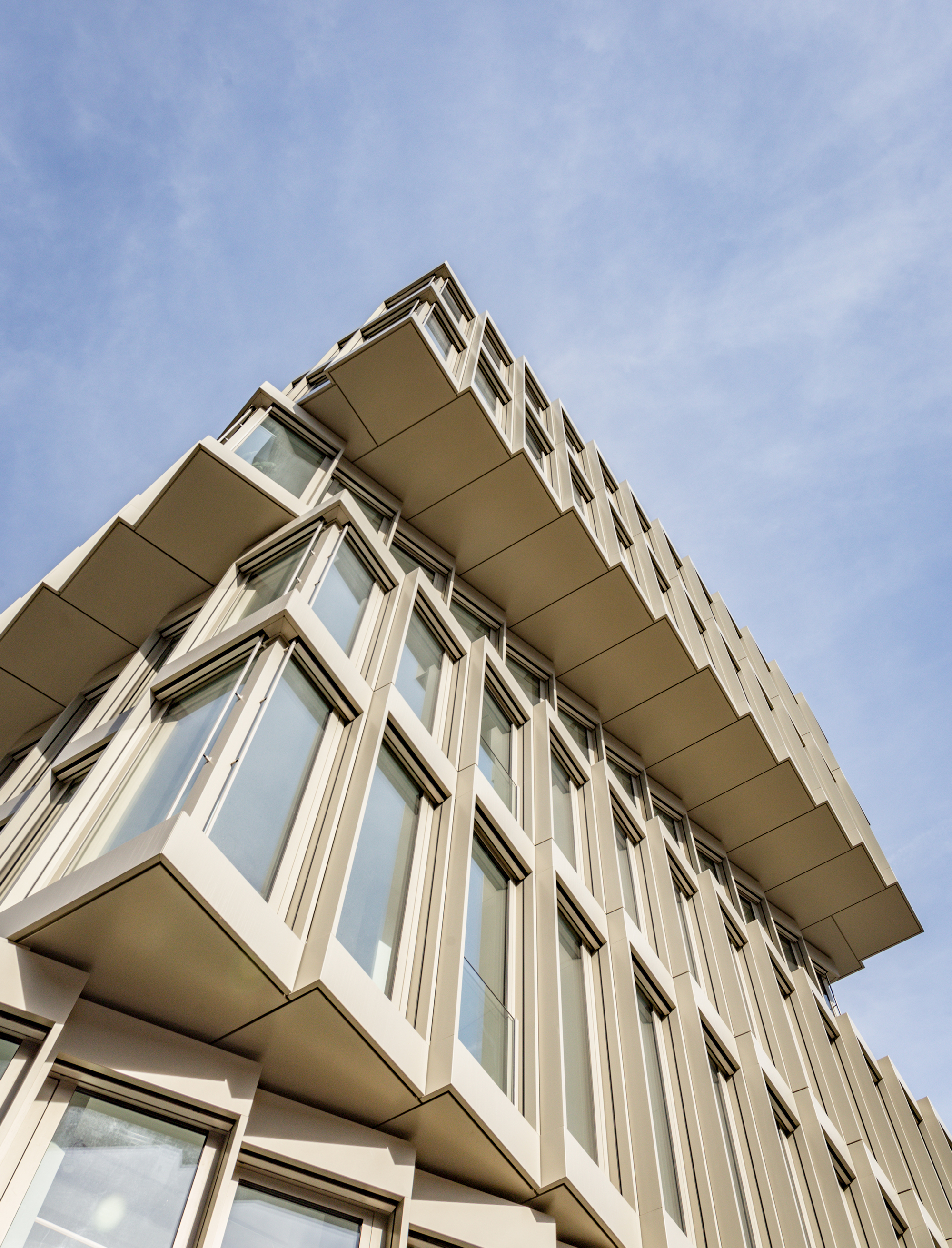 Upward view of cantilevered corner with protruding window bays and deep recessed soffits against blue sky