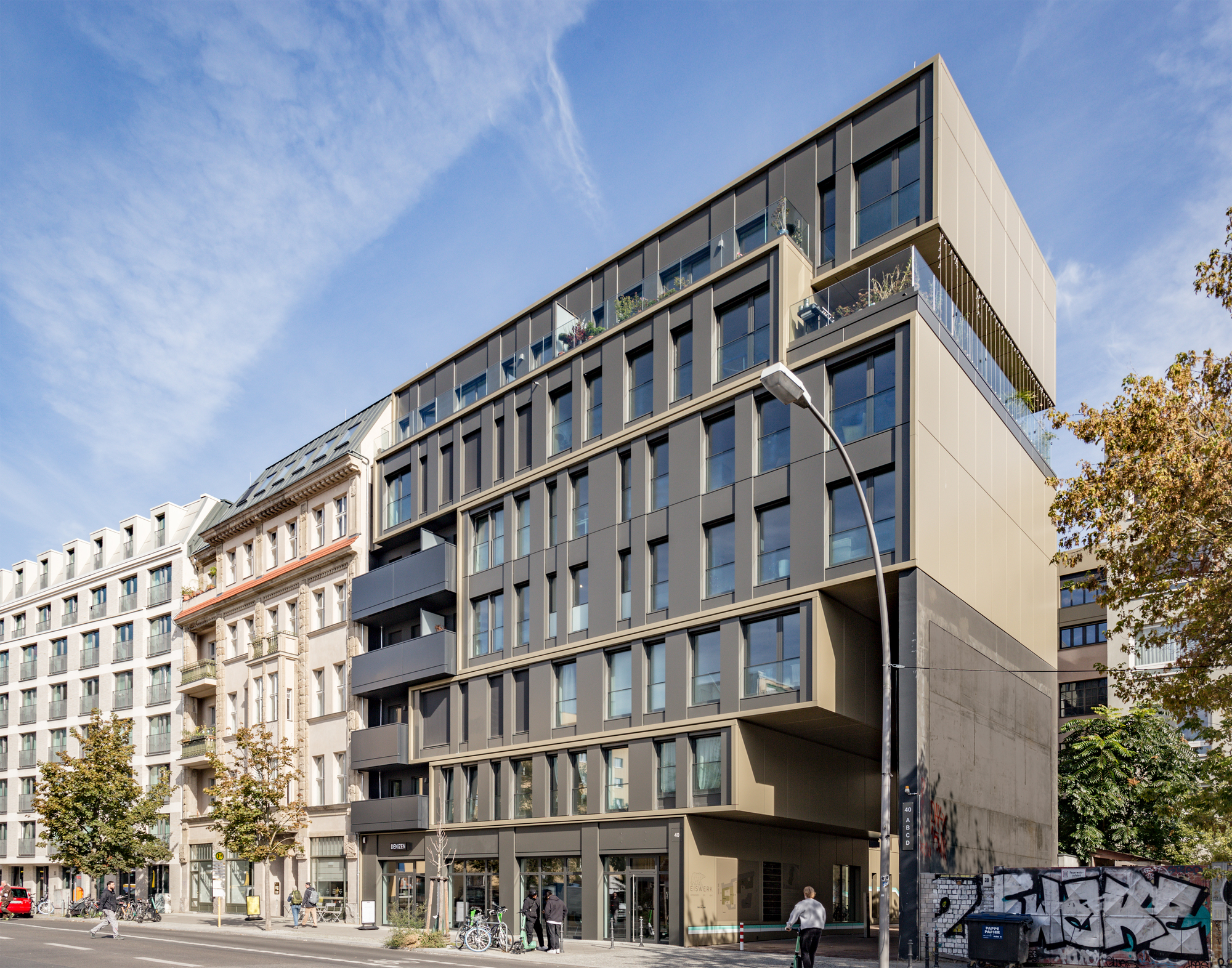 Street facade showing cantilevered volumes above ground-level retail with pedestrians and bicycles passing by
