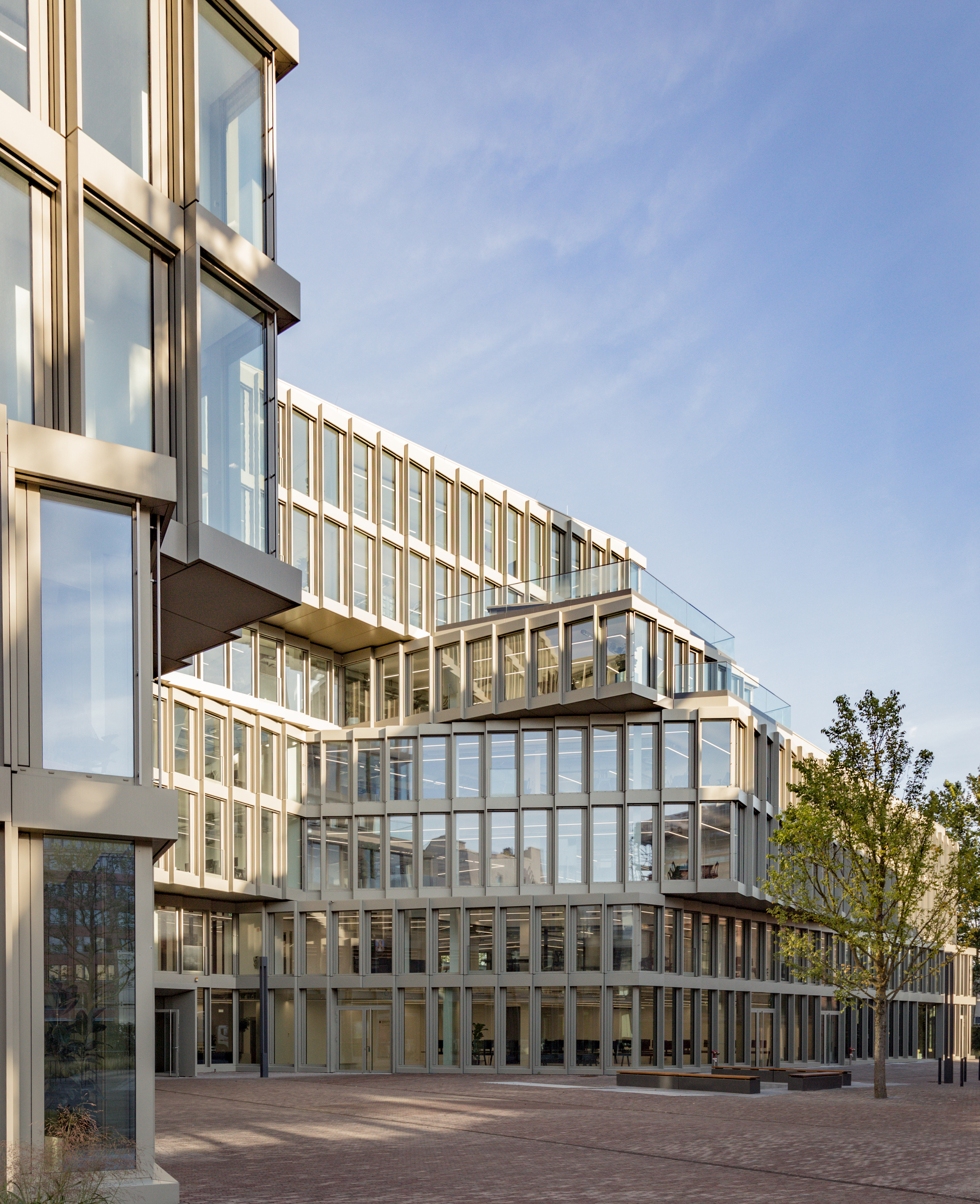 Courtyard view of the terraced glass and metal facade under afternoon light with trees