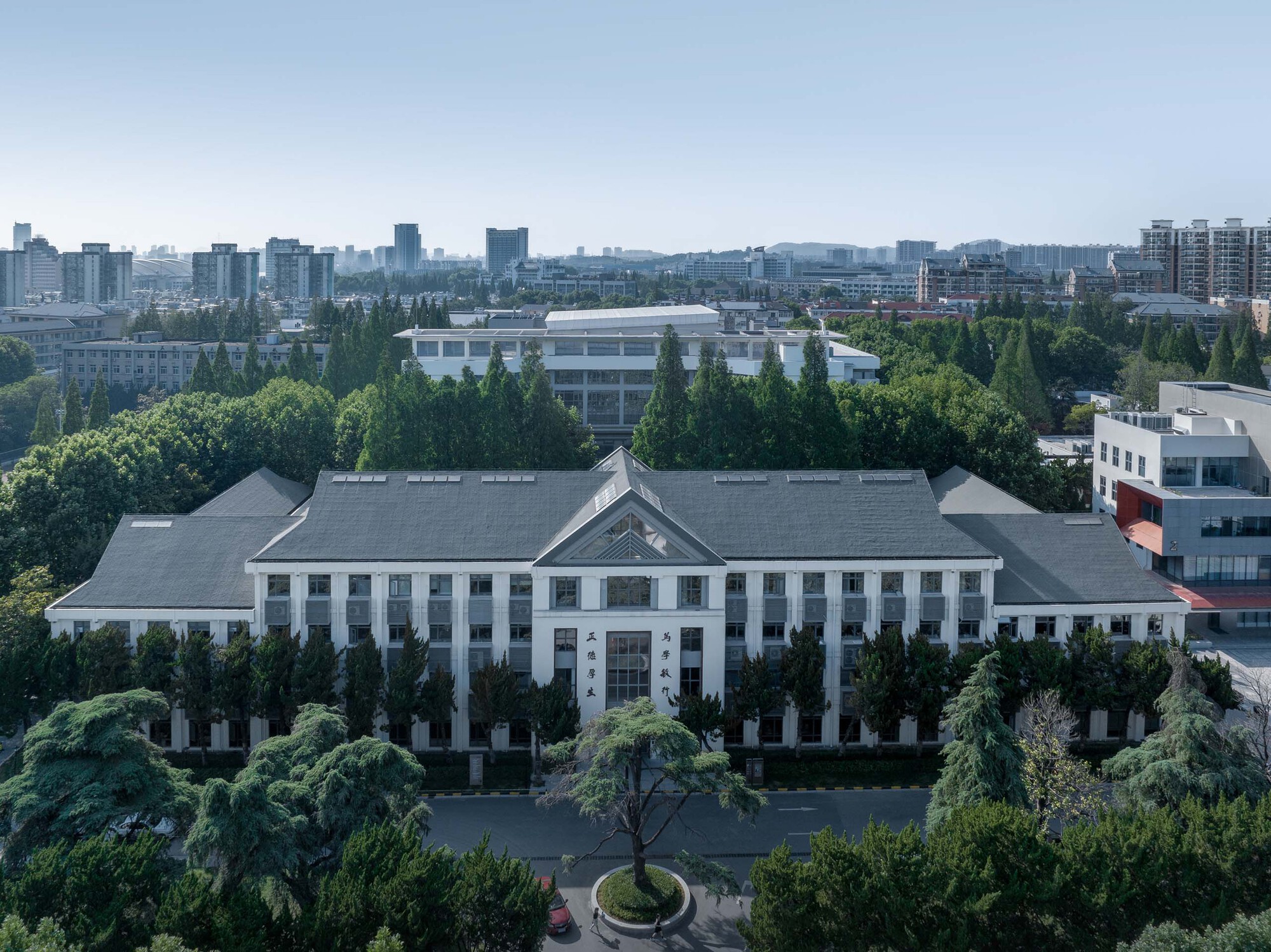 Aerial view of the white symmetrical facade with central pediment surrounded by dense green trees