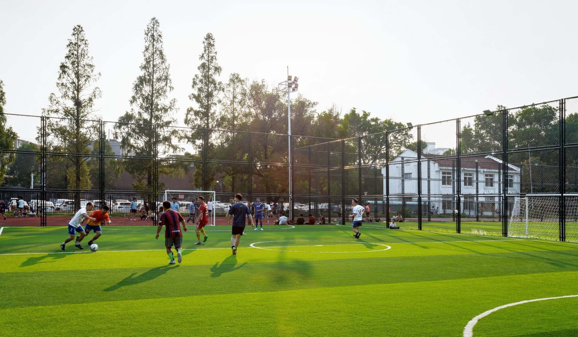 Synthetic turf sports pitch with mesh fencing and players in afternoon light
