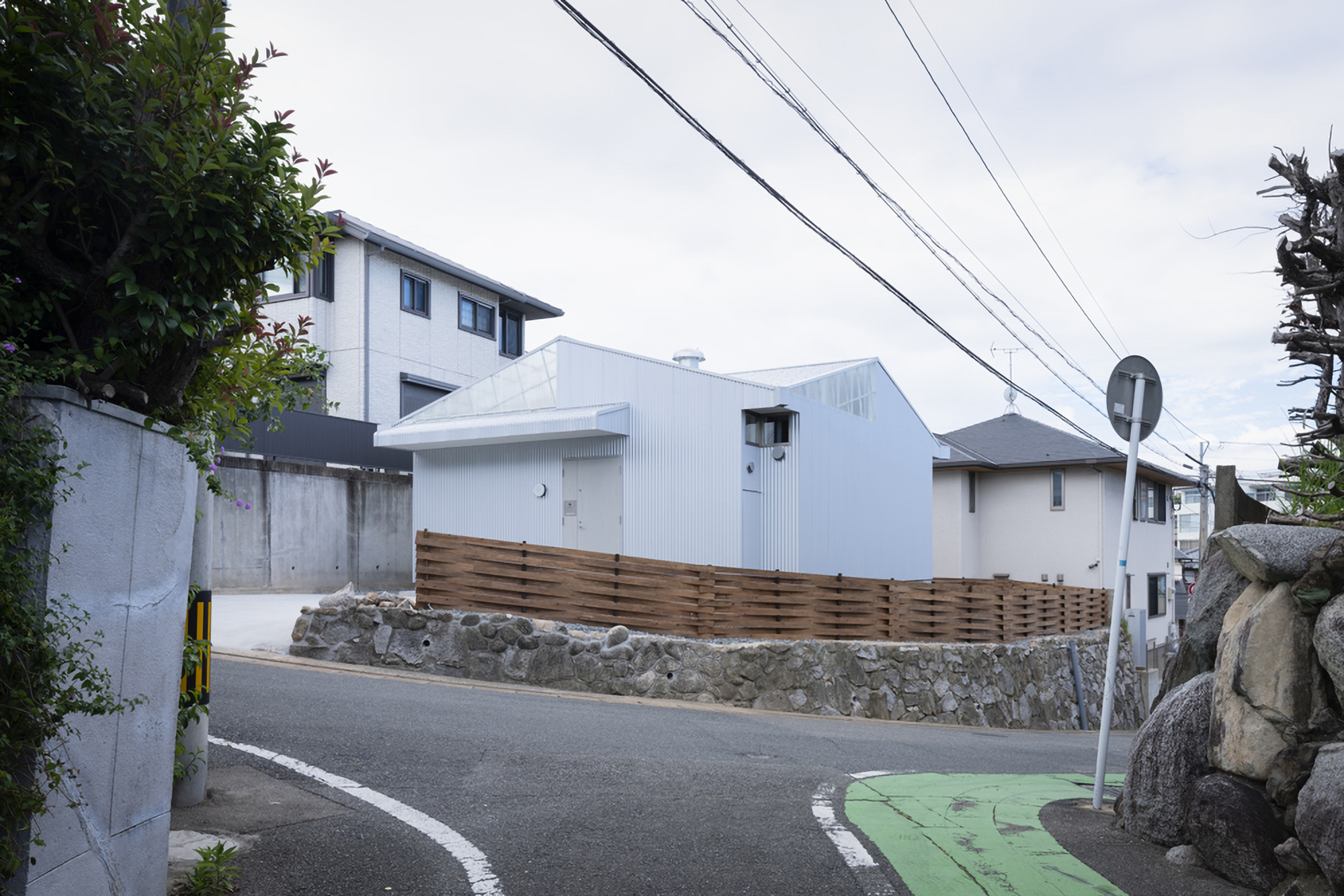 Street view with overhead power lines and timber fence screening the white corrugated metal structure