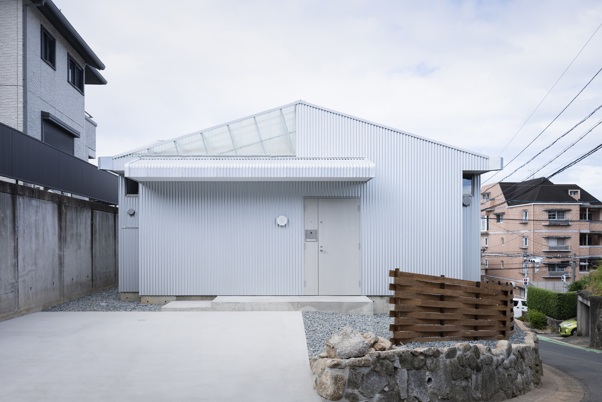 White corrugated metal facade with gabled roof and clerestory windows facing a gravel courtyard