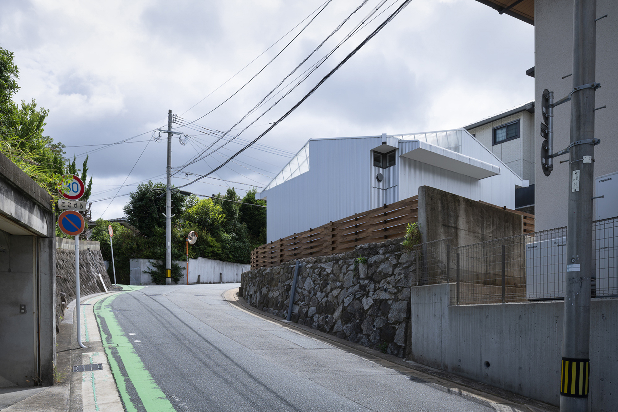 Sloping neighborhood street with the house set behind stone and timber boundary walls