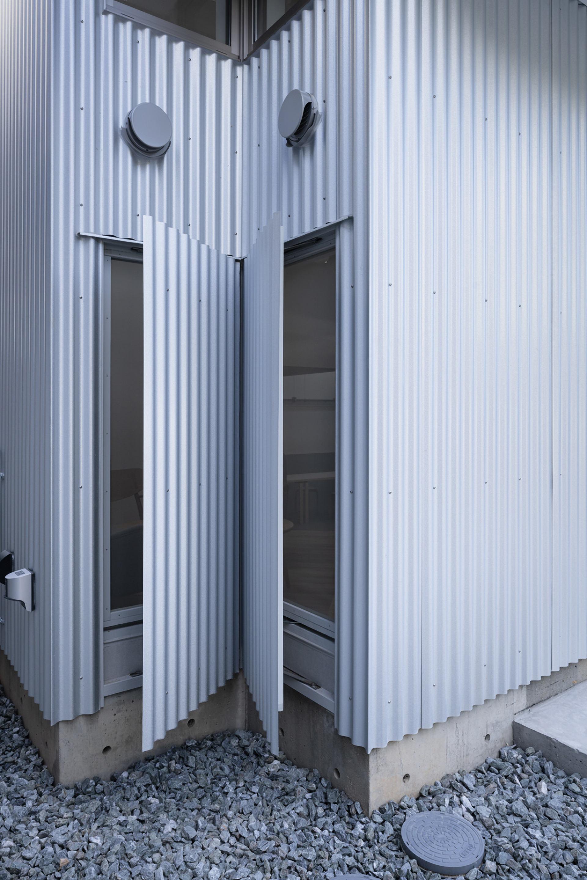 Corner detail of the corrugated metal cladding with glazed door openings and exposed concrete base