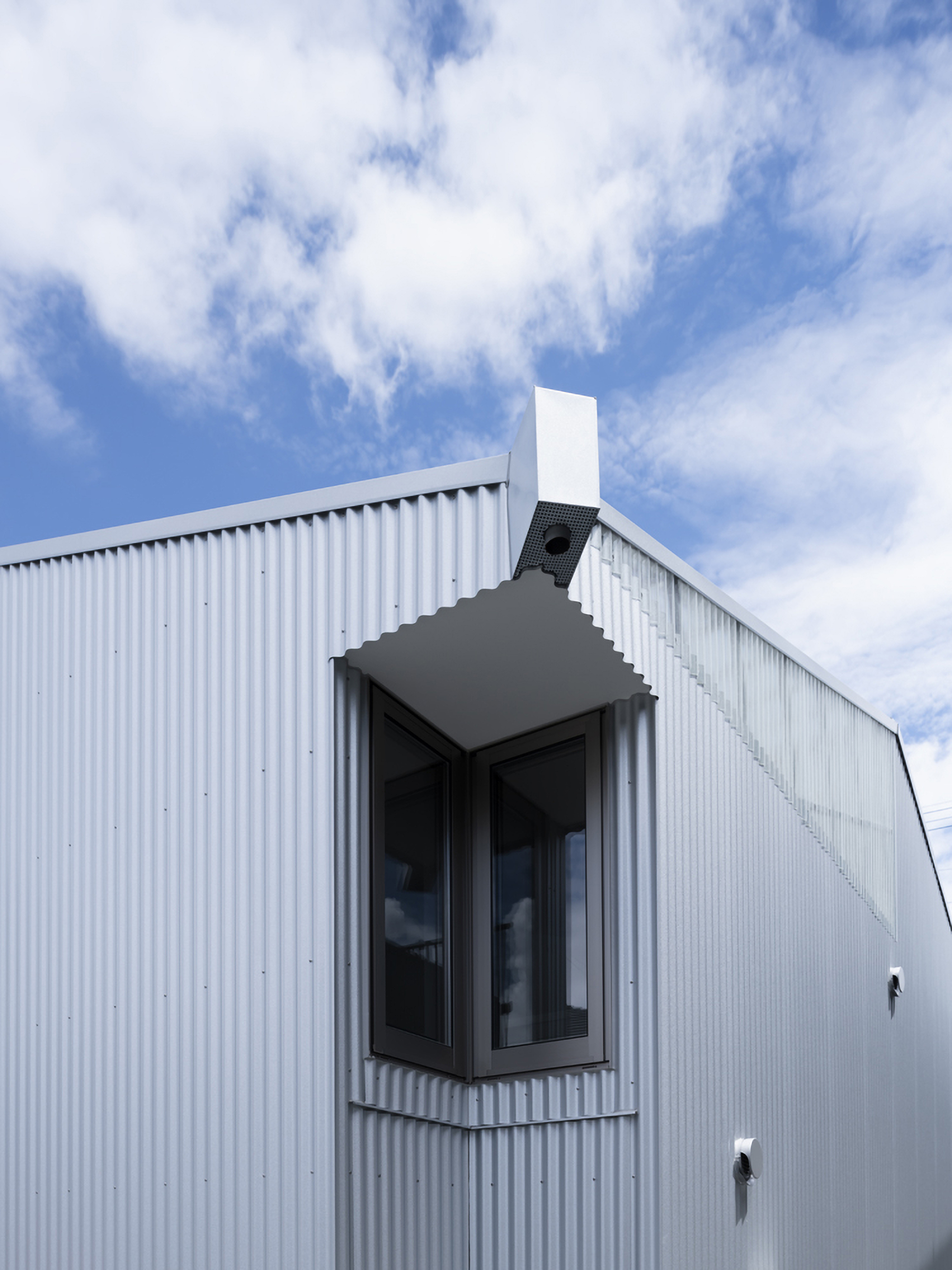 Projecting window box with metal hood and white chimney against blue sky with clouds