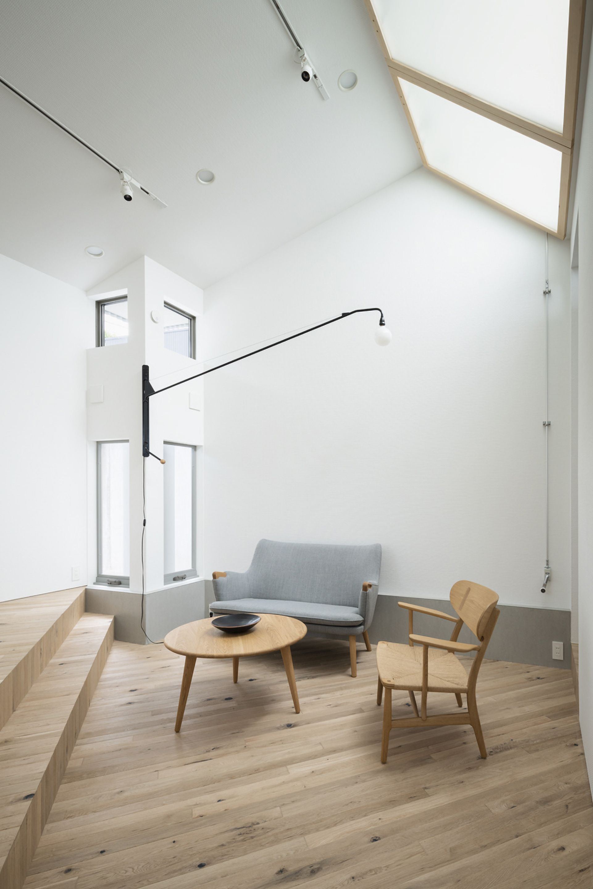 Double-height living room with timber-framed skylights and a grey sofa beneath tall windows