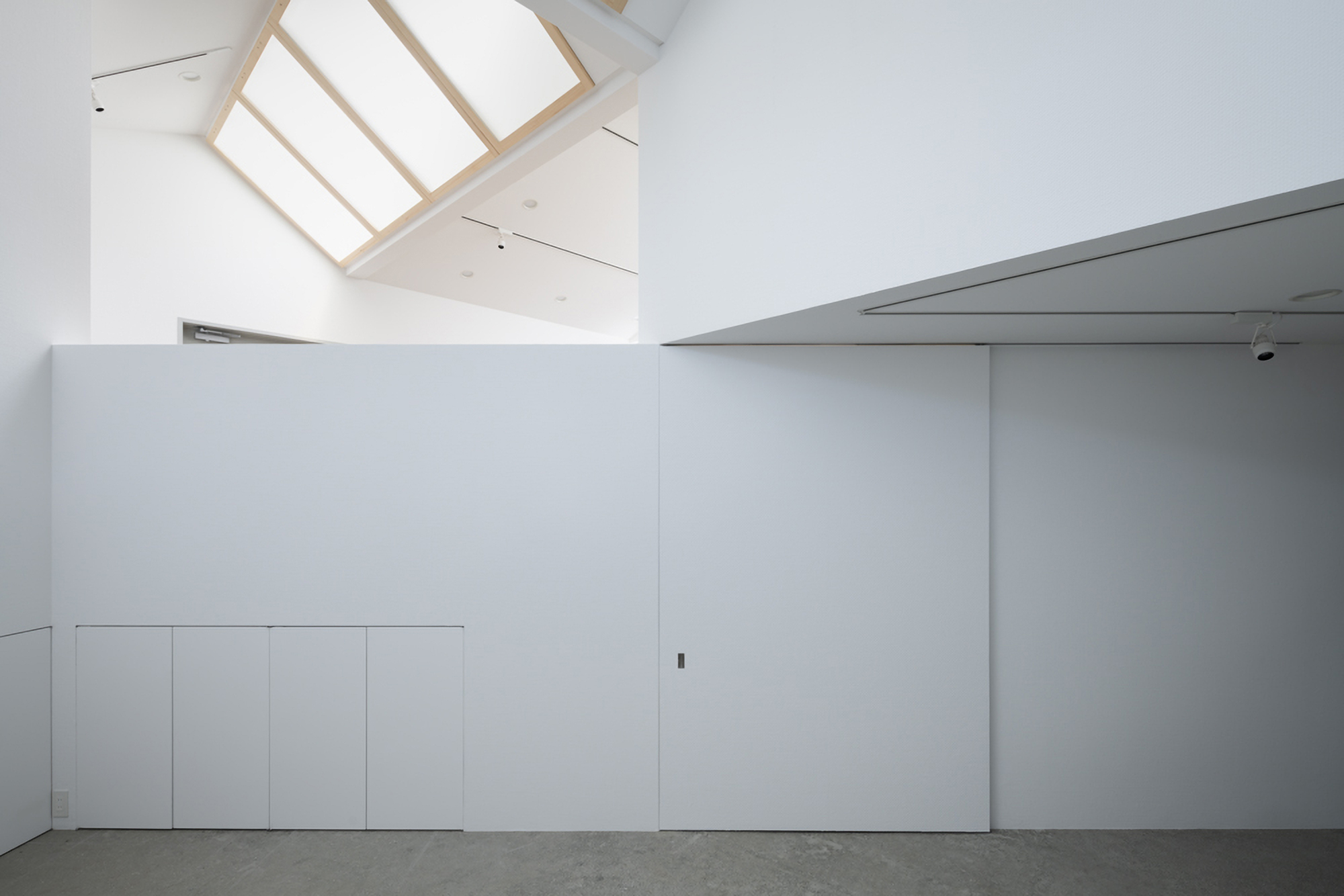 Minimalist white storage wall with polished concrete flooring and recessed ceiling panels